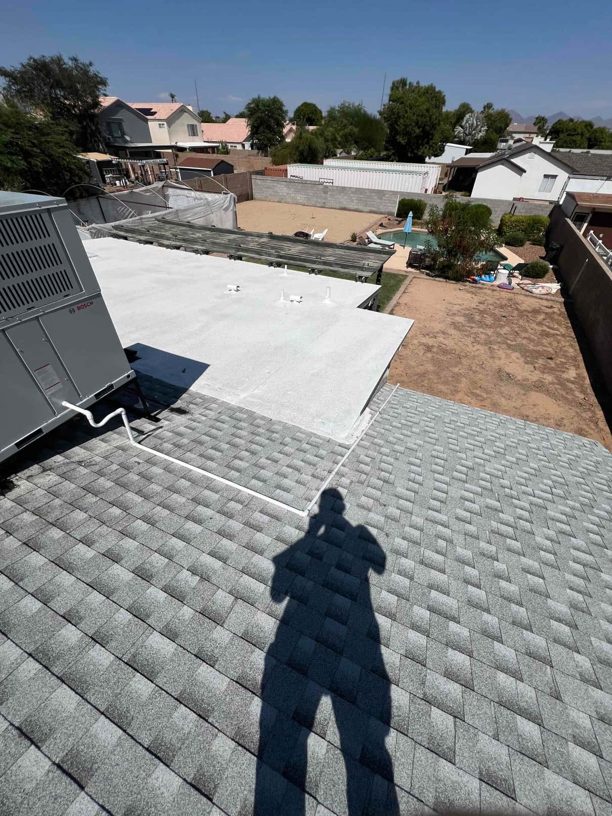 Rooftop package unit installed with new condensate drain routing across shingles and onto coated flat roof section.