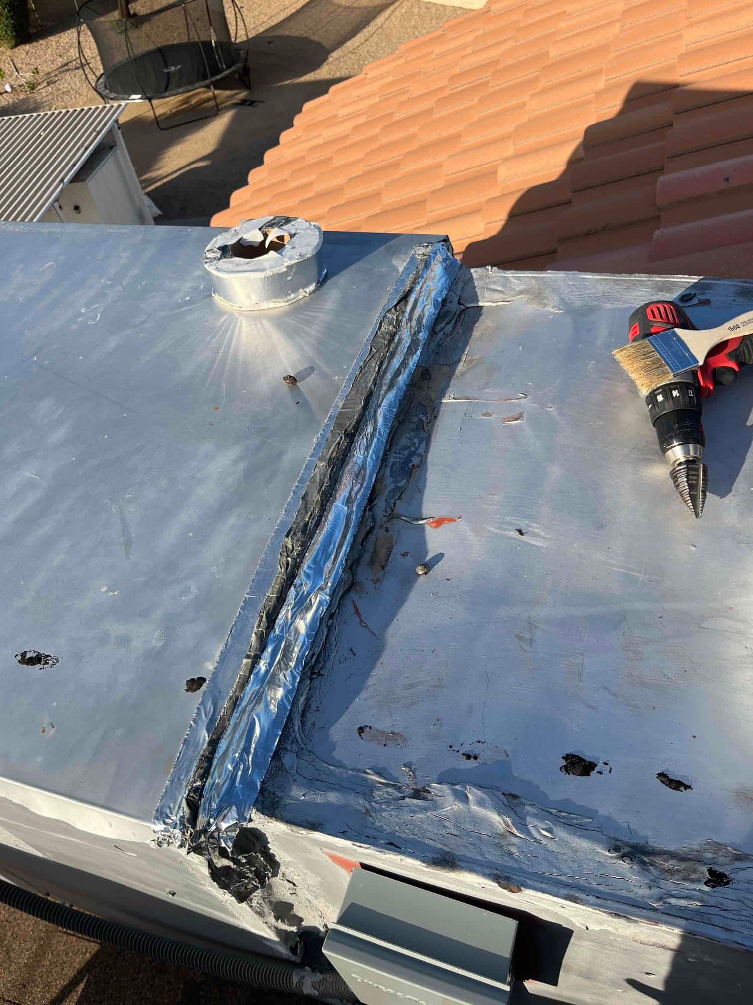 Rooftop package unit top panel with deteriorated seam sealant and multiple fastener holes near a cordless drill.