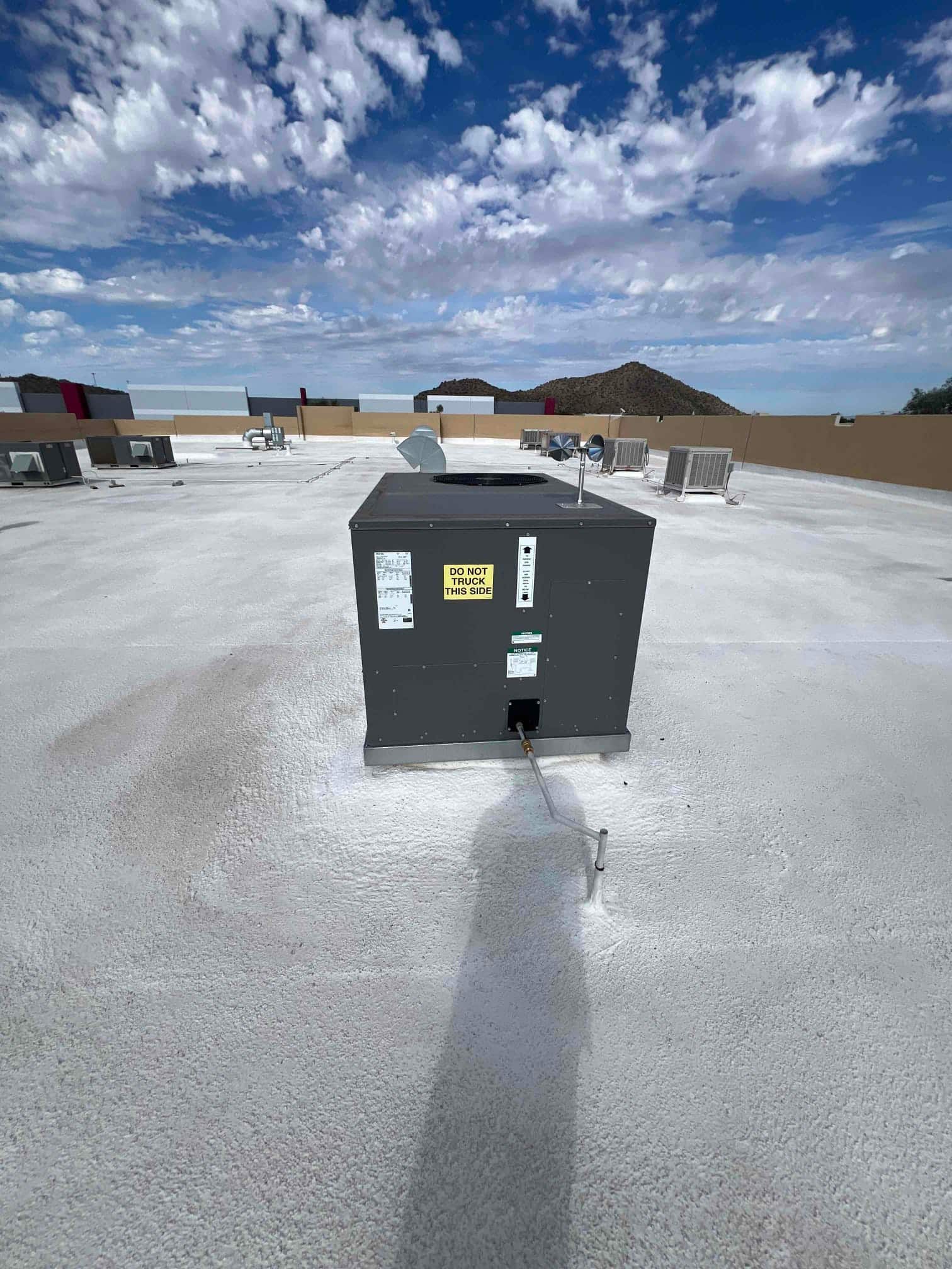 Rooftop packaged HVAC unit newly installed on a coated roof, with line set penetration sealed and surrounding equipment visible.