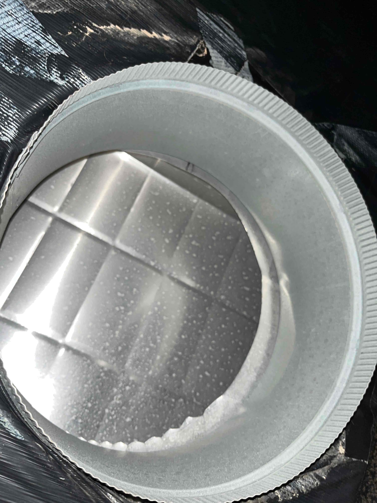 Round flexible HVAC duct with inner liner and condensation droplets visible on the reflective vapor barrier surface.