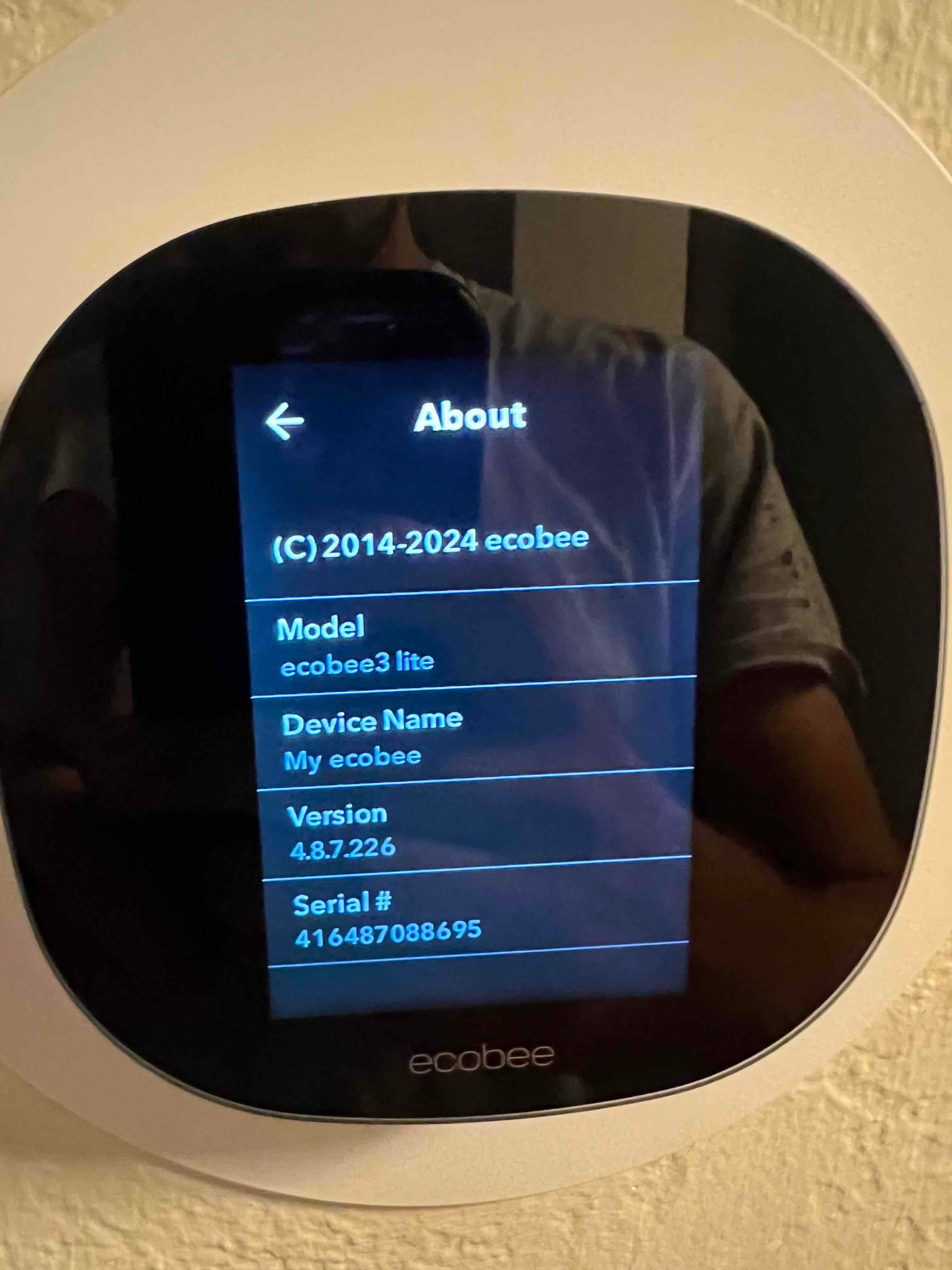 Smart thermostat mounted on wall displaying device information screen during setup after HVAC installation.