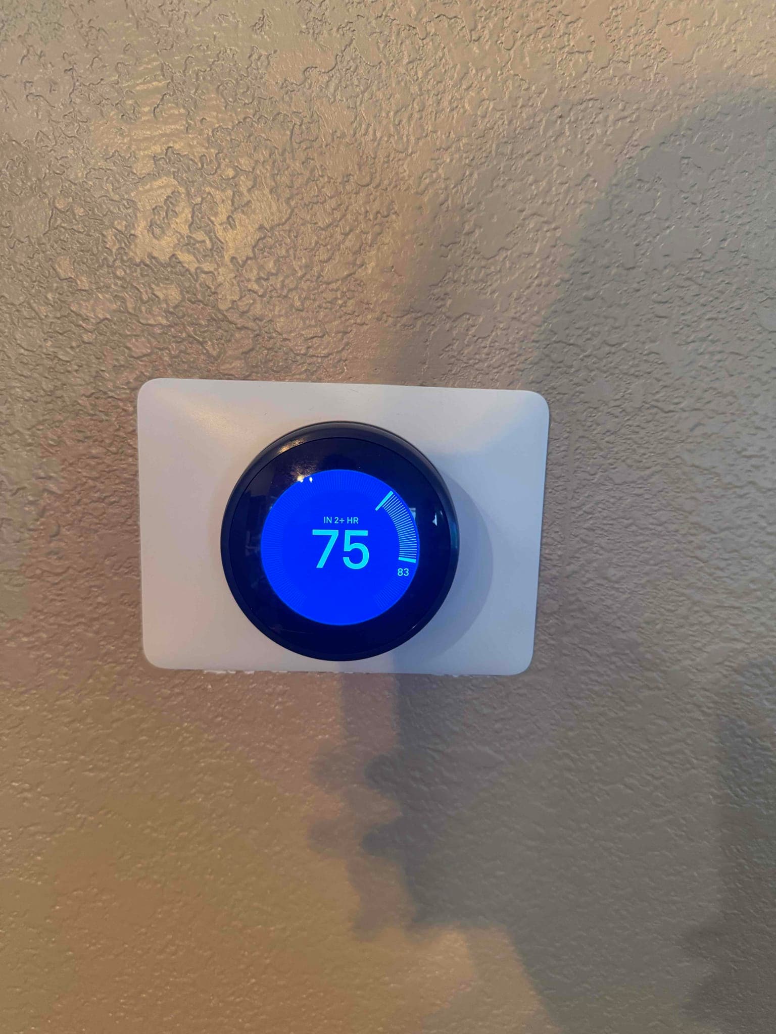 Smart thermostat on a textured interior wall displays a setpoint of 75 degrees with cooling active.