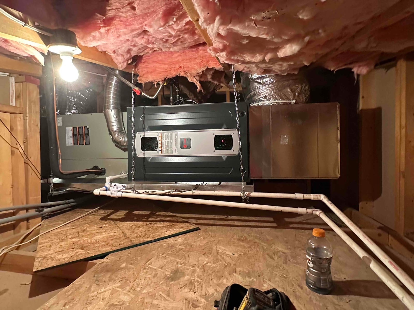 Suspended air handler and furnace installation with duct connections, condensate drain piping, and insulated refrigerant lines in an attic space.