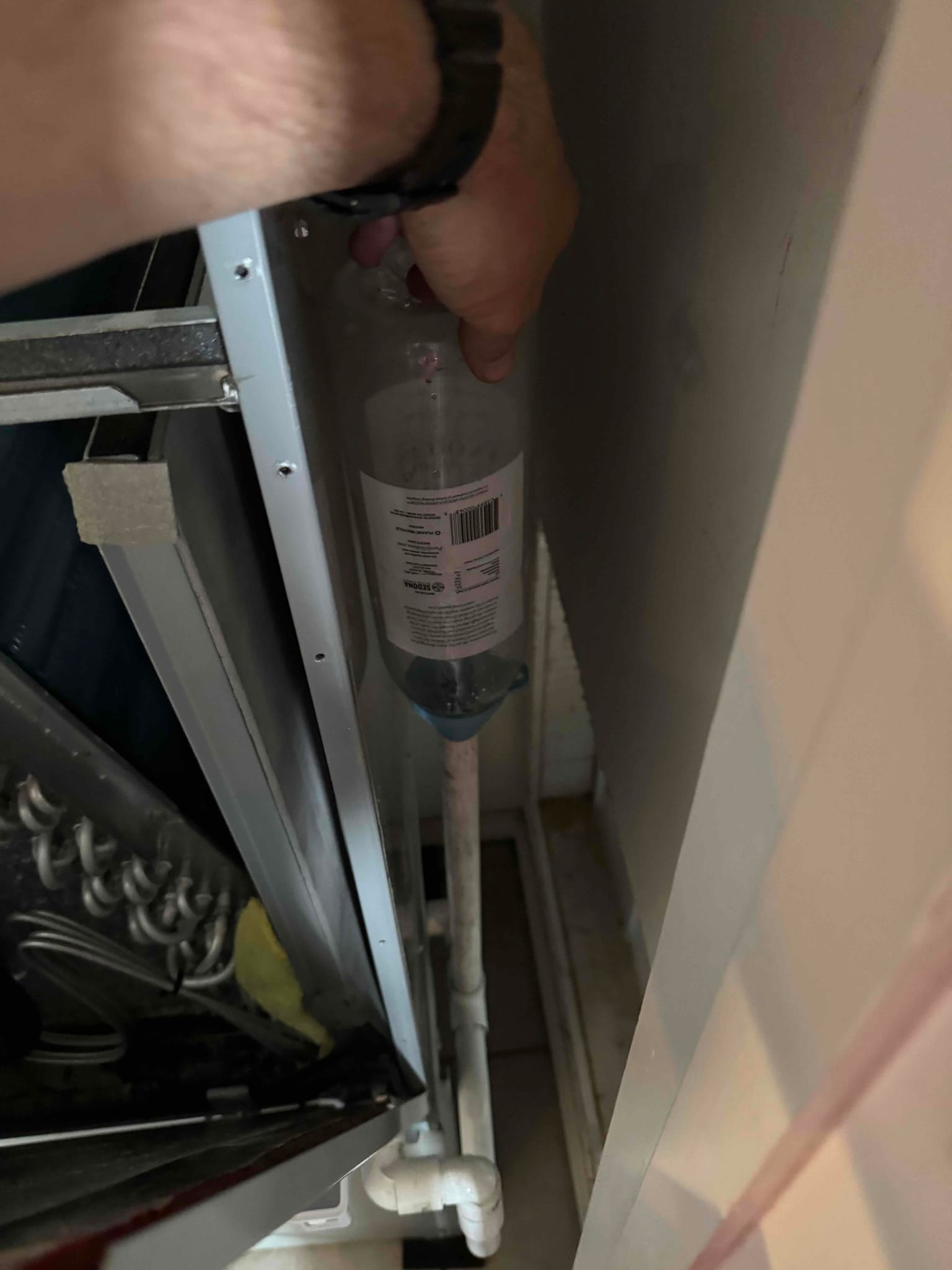 Technician flushes the condensate drain line with a squeeze bottle at the air handler’s drain connection.