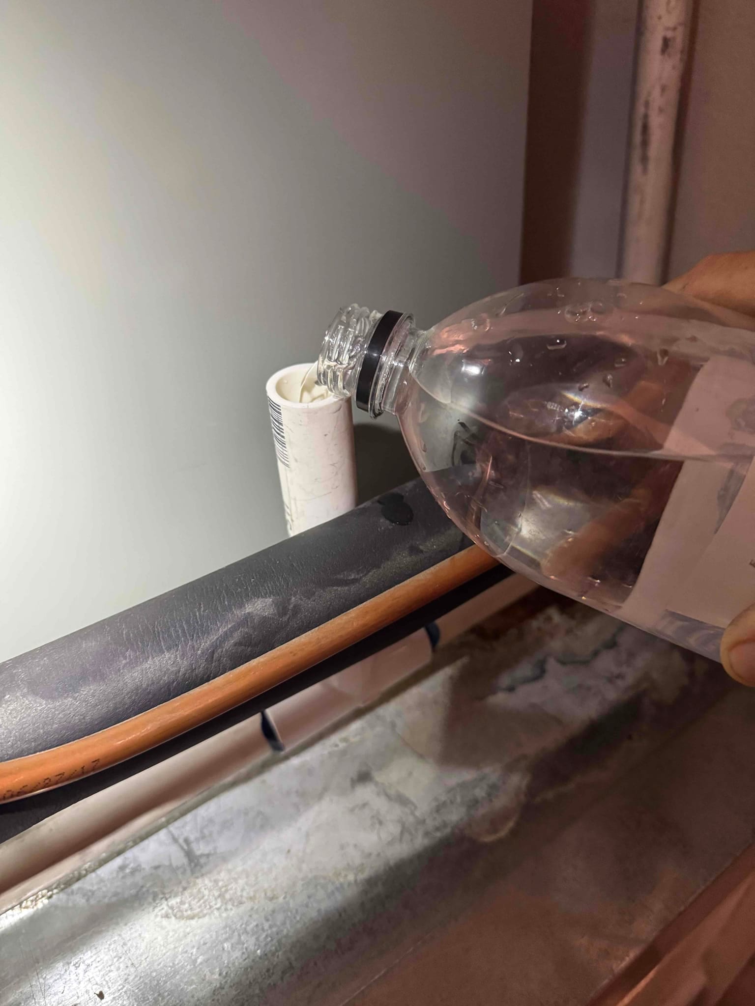 Technician pours cleaning solution into a PVC condensate drain line to flush and clear buildup.