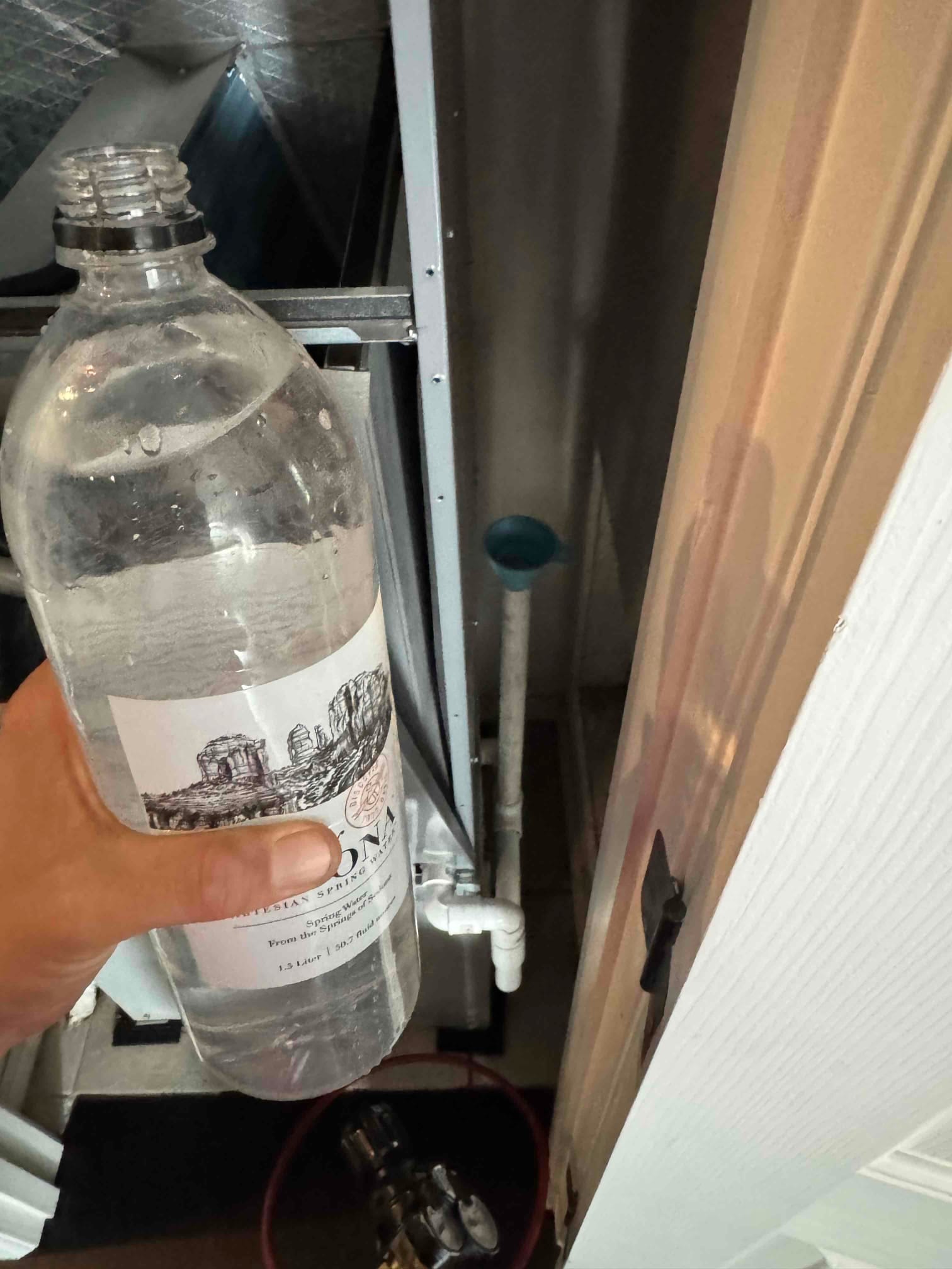Technician pours water into the condensate drain cleanout to flush and test the air handler’s drain line.