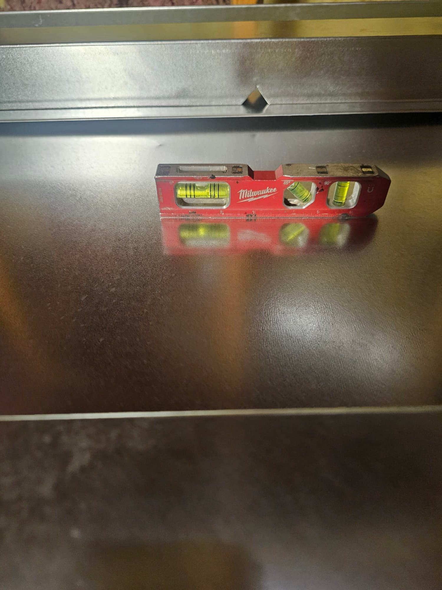 Torpedo level placed on newly installed sheet-metal plenum or duct surface to verify it is set perfectly level.