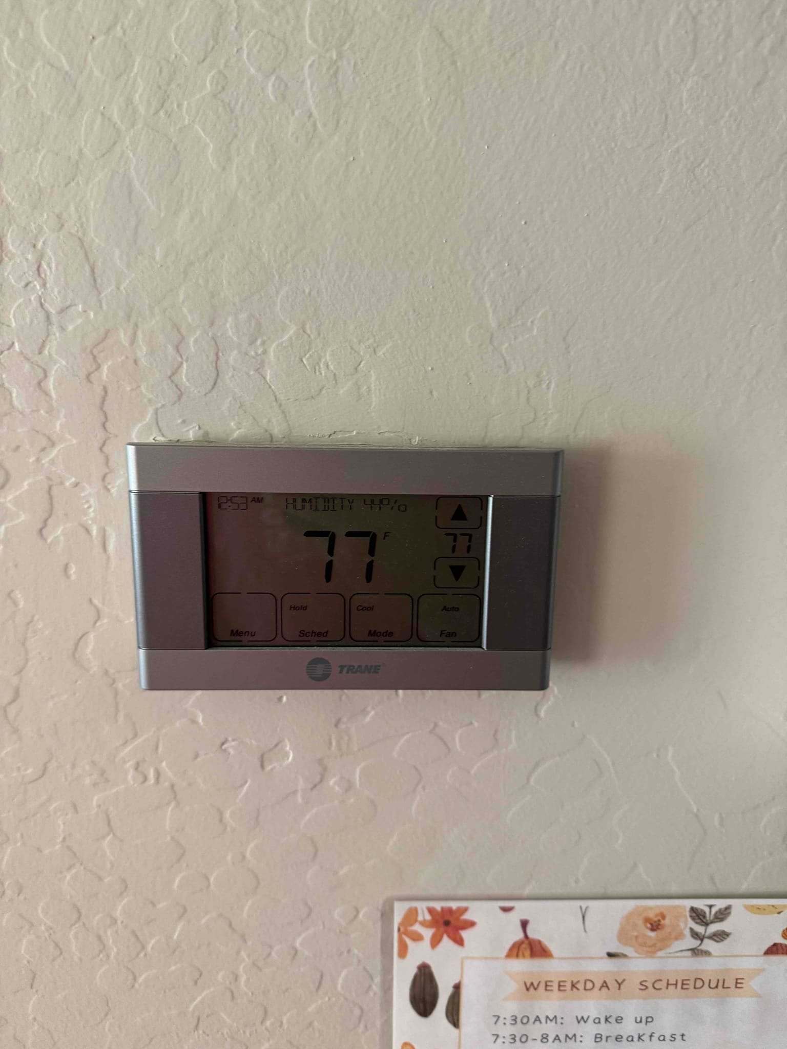 Wall-mounted digital thermostat displaying 77 degrees with control buttons and icons visible on the screen.