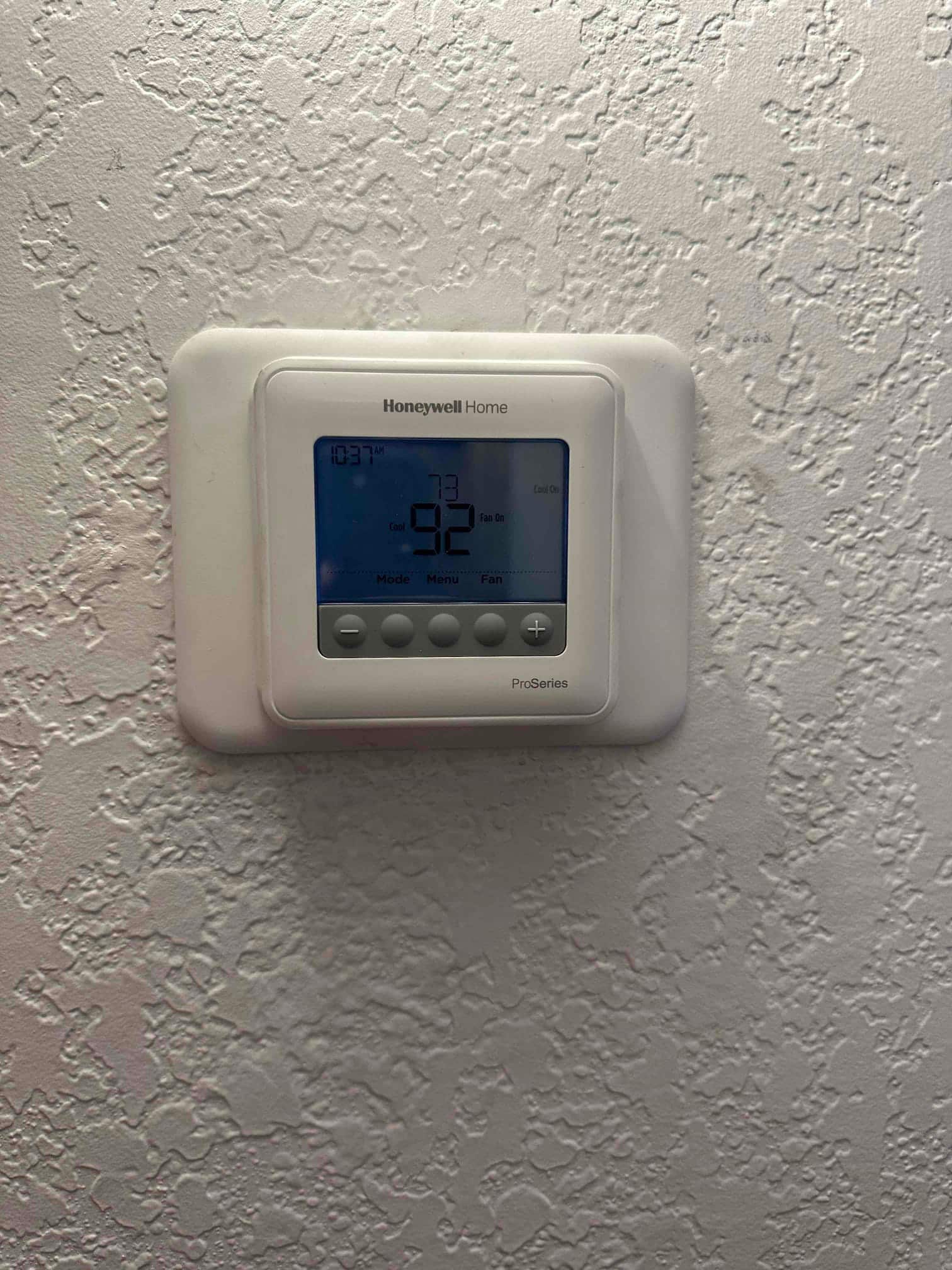 Wall-mounted digital thermostat installed and operating, display illuminated with system mode and fan status indicators.