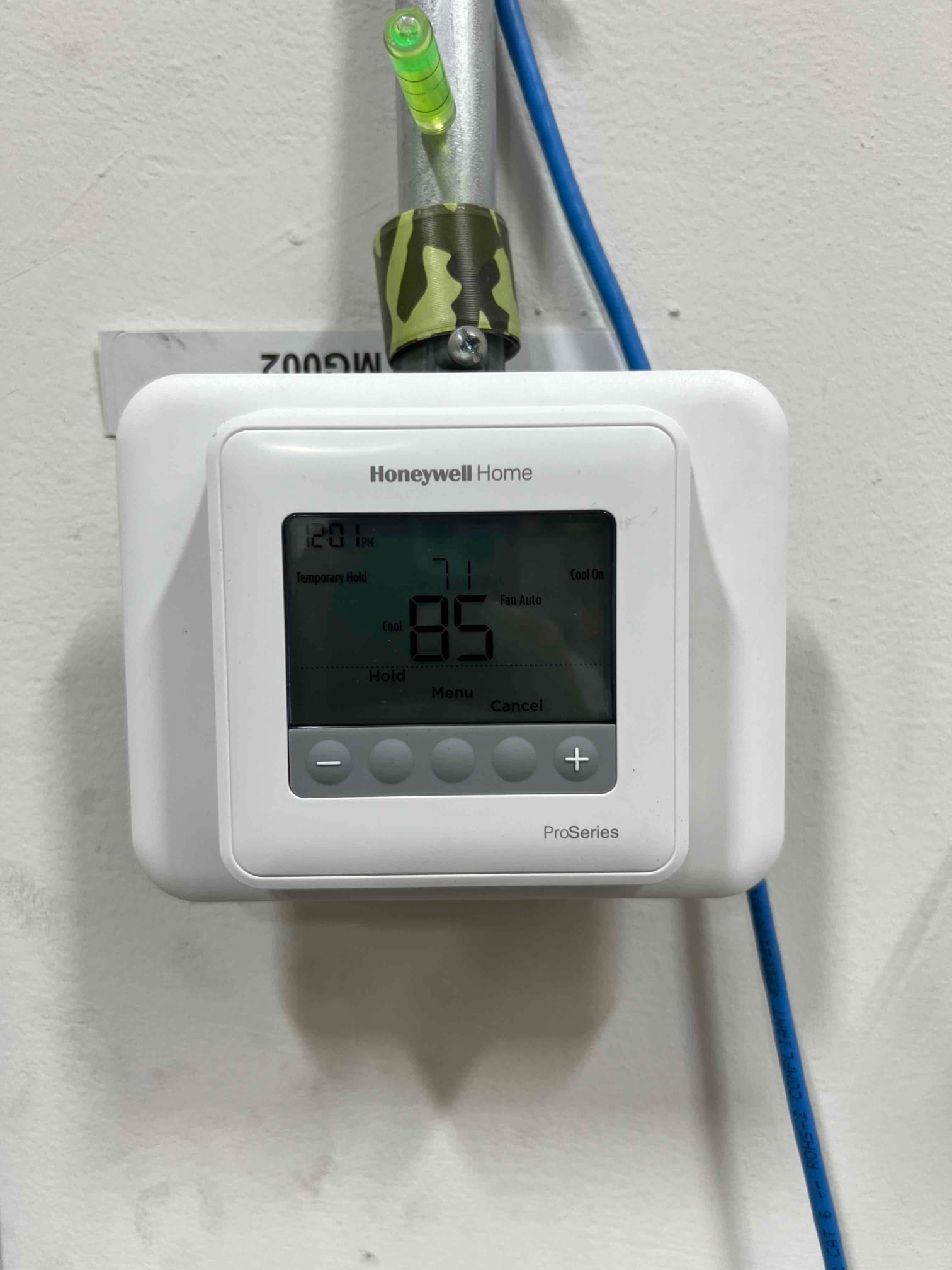 Wall-mounted digital thermostat installed and powered, displaying system mode and temperature with conduit and low-voltage cable routed neatly.