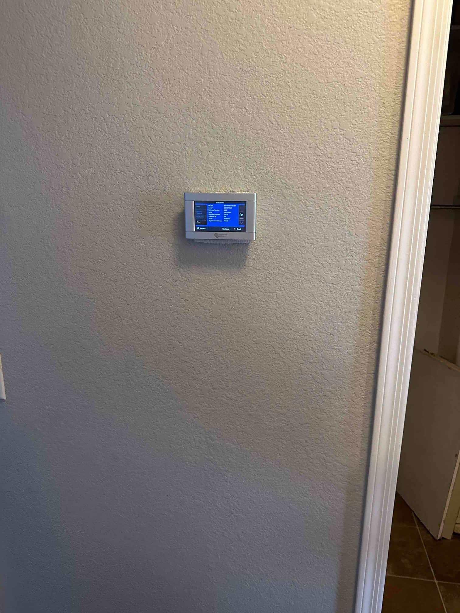 Wall-mounted digital thermostat installed and powered on, displaying system menu during commissioning of the new HVAC system.