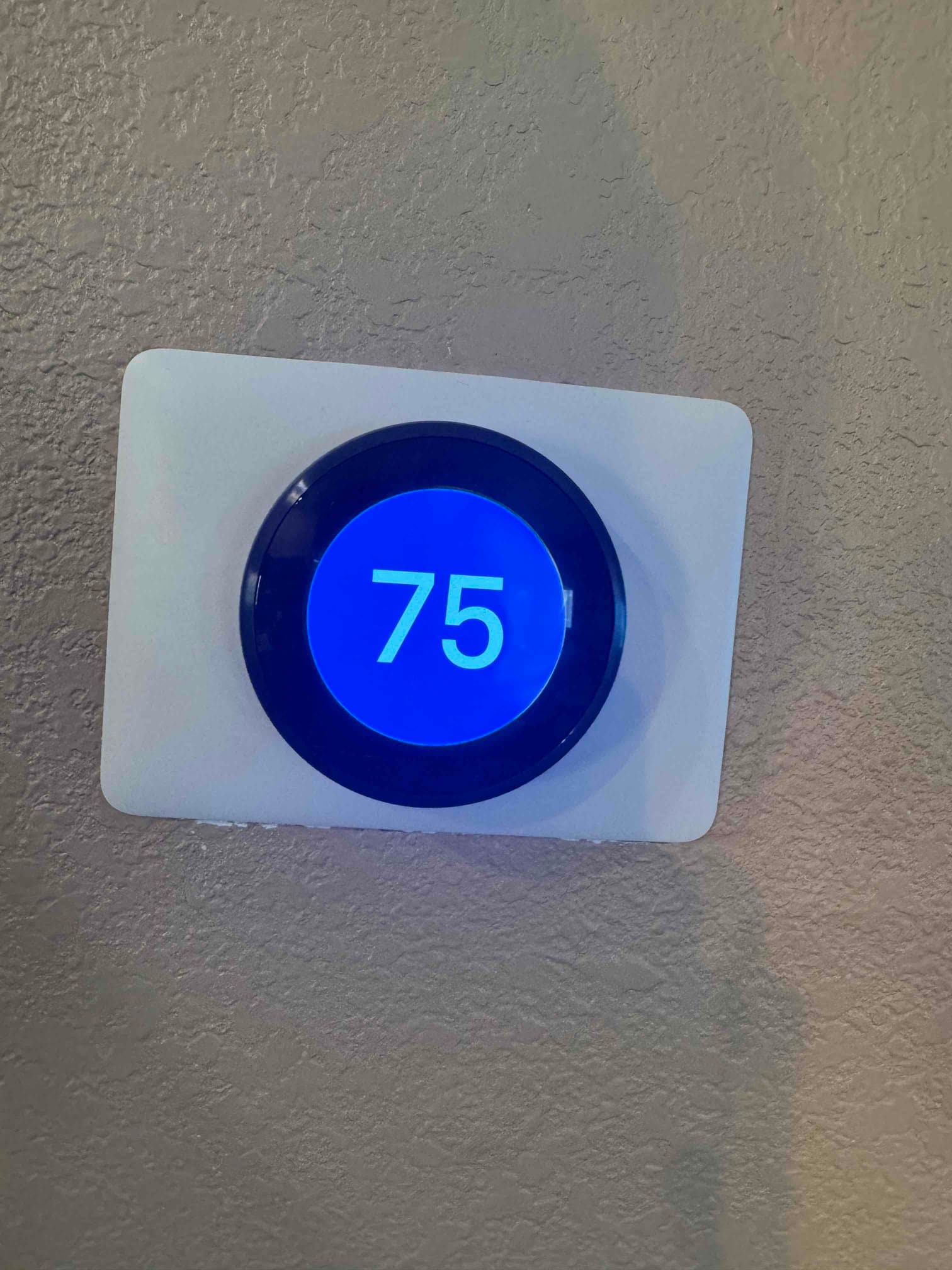 Wall-mounted digital thermostat shows 75°F on the display during air conditioning repair visit.