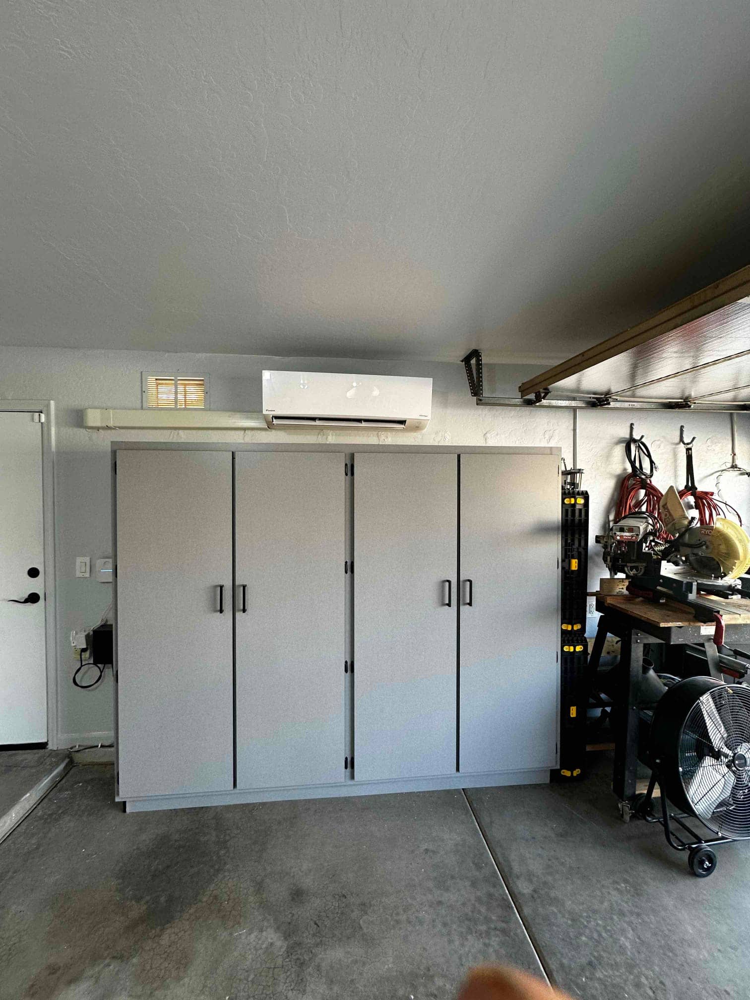 Wall-mounted mini-split indoor unit installed above garage cabinets with line set cover neatly routed along the wall.