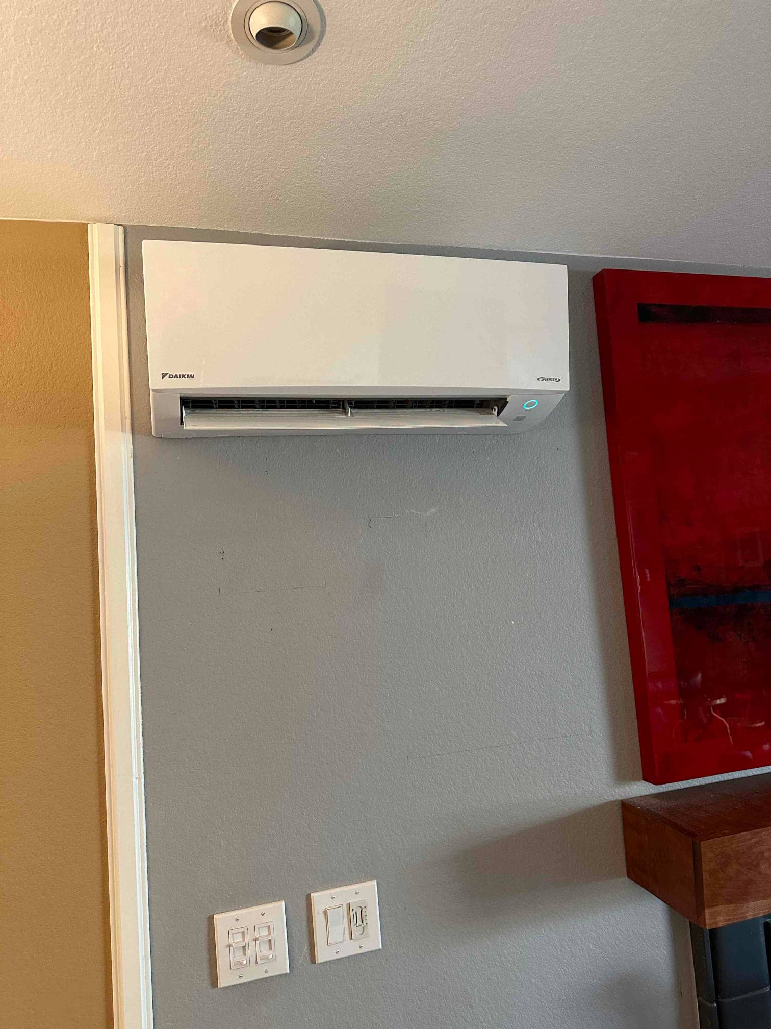 Wall-mounted mini-split indoor unit installed and operating, with louver open and indicator light on above nearby wall switches.