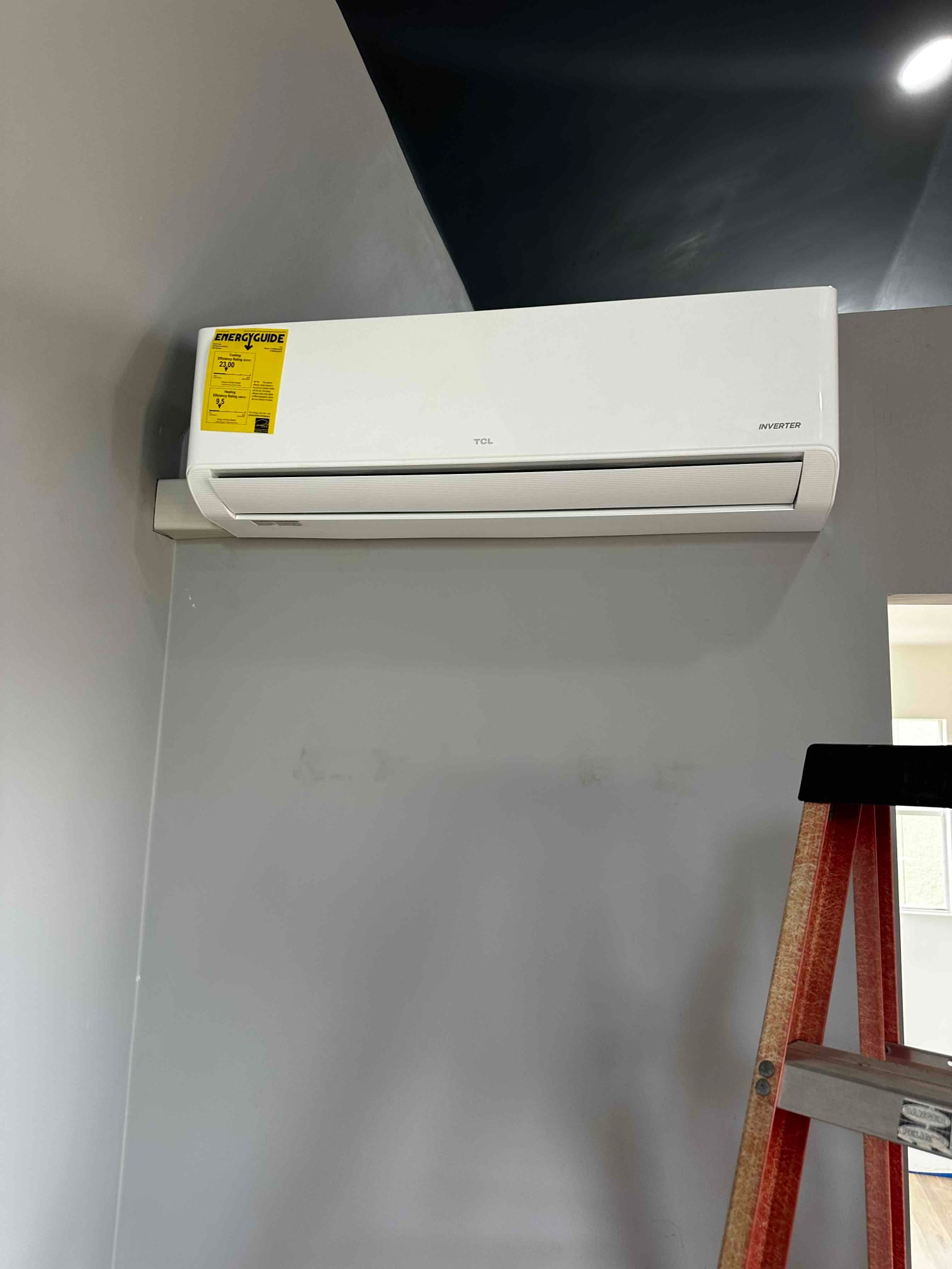 Wall-mounted mini-split indoor unit newly installed on a finished wall, with ladder nearby for access during installation.