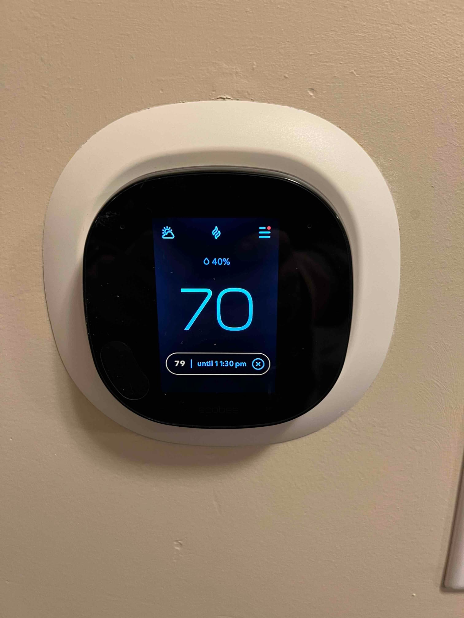 Wall-mounted smart thermostat displaying 70 degrees with humidity indicator, installed on a finished interior wall.