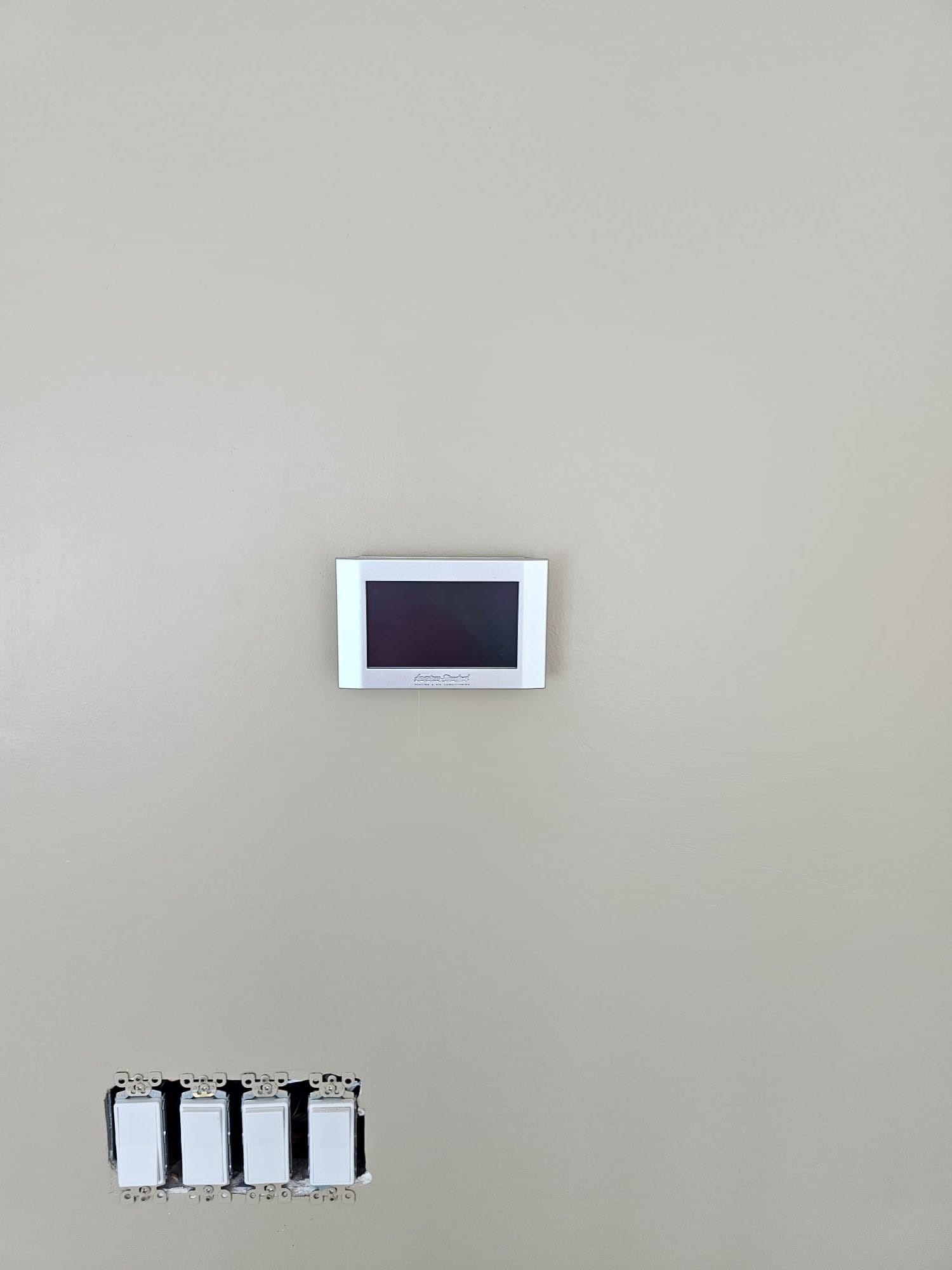 Wall-mounted thermostat installed above a bank of electrical switches, showing the completed control interface for the new HVAC system.