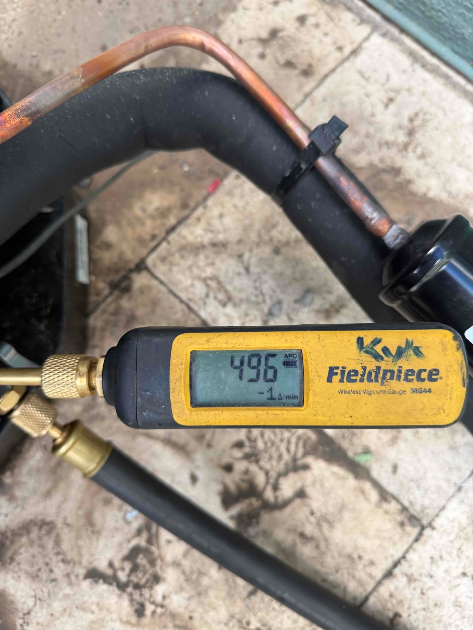 Digital micron gauge connected to the system shows 496 microns, confirming a deep vacuum during evacuation before refrigerant charging.