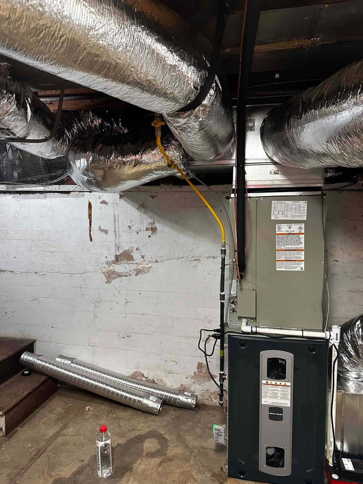 New furnace and coil installed with insulated supply and return ducts connected, gas line, condensate drain, and electrical whip routed.