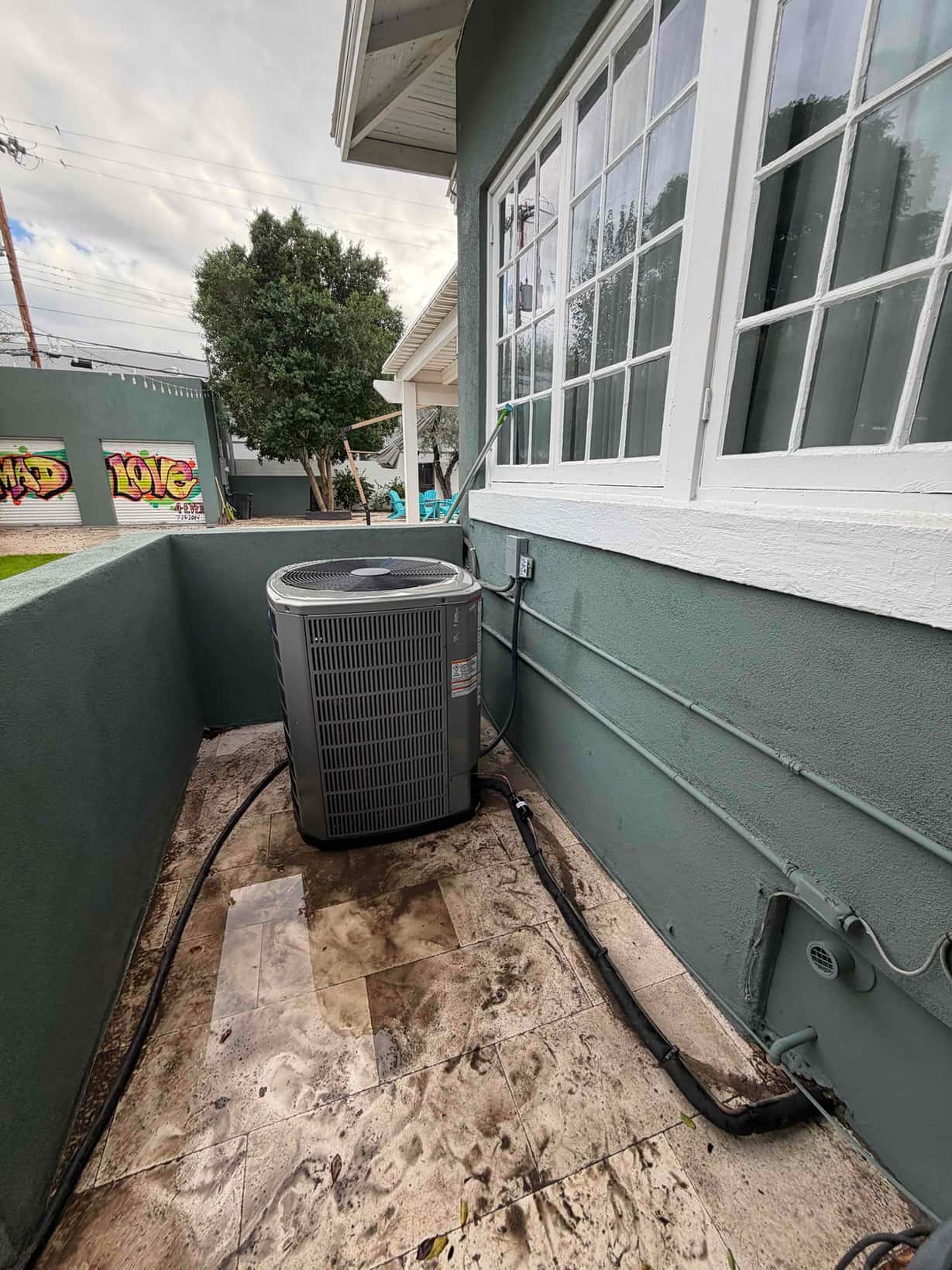 New outdoor condenser installed on a level pad with insulated refrigerant line set routed along the wall to the penetration.