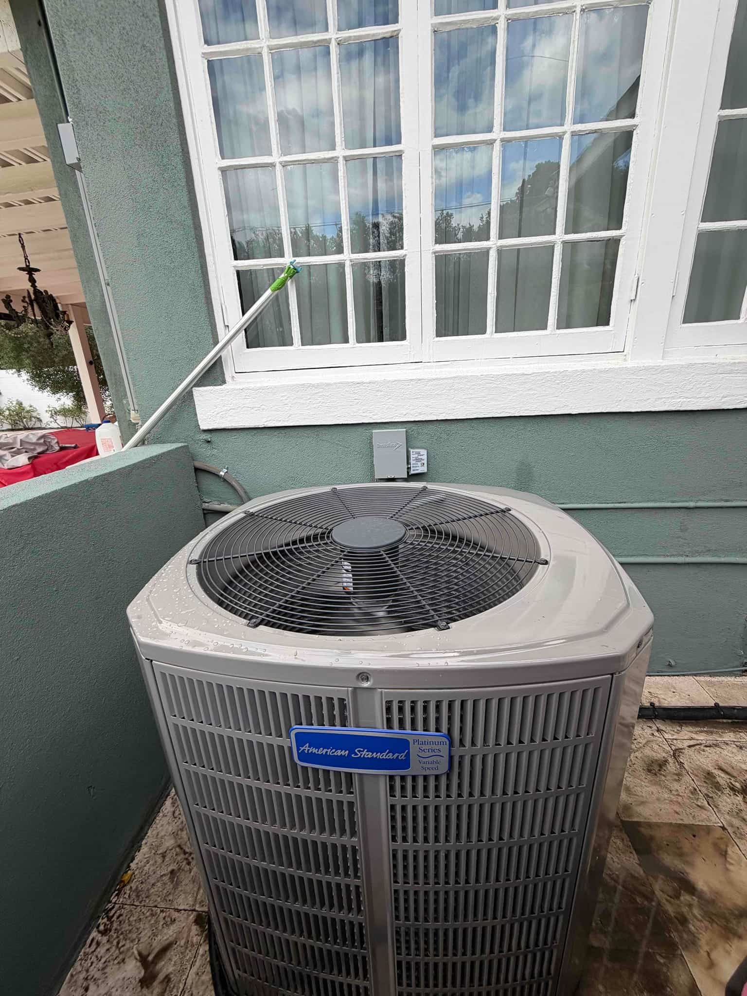 New outdoor condenser set beside the house with disconnect box mounted and refrigerant lines routed along the wall.