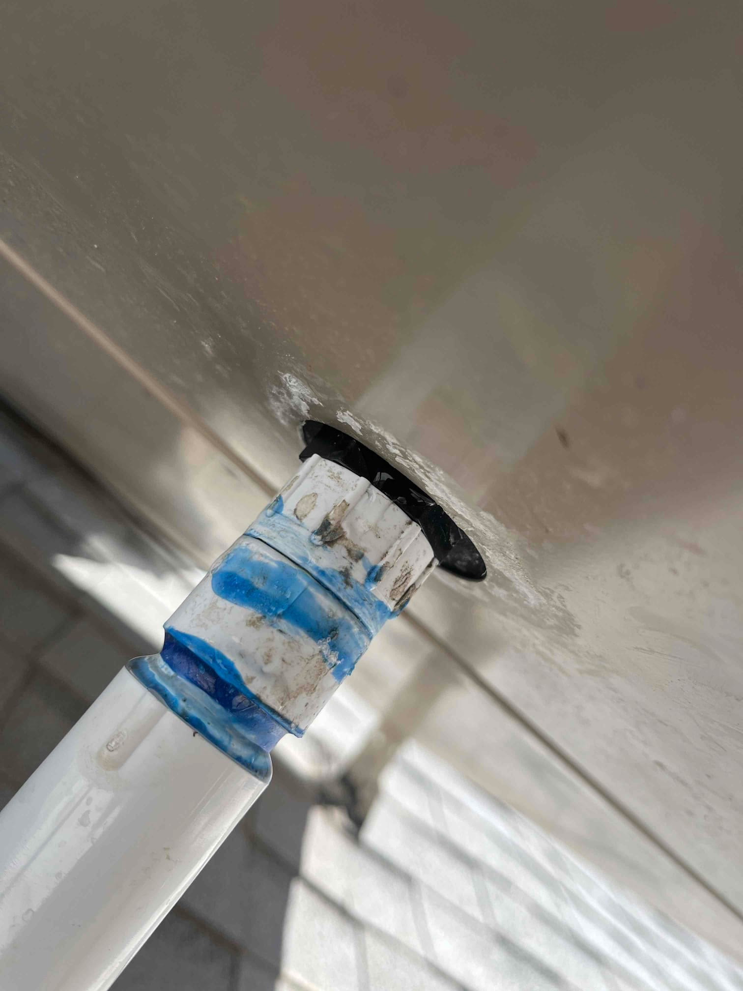 Close-up of an evaporative cooler stand pipe connection with new PVC fitting and rubber grommet sealed at the basin.