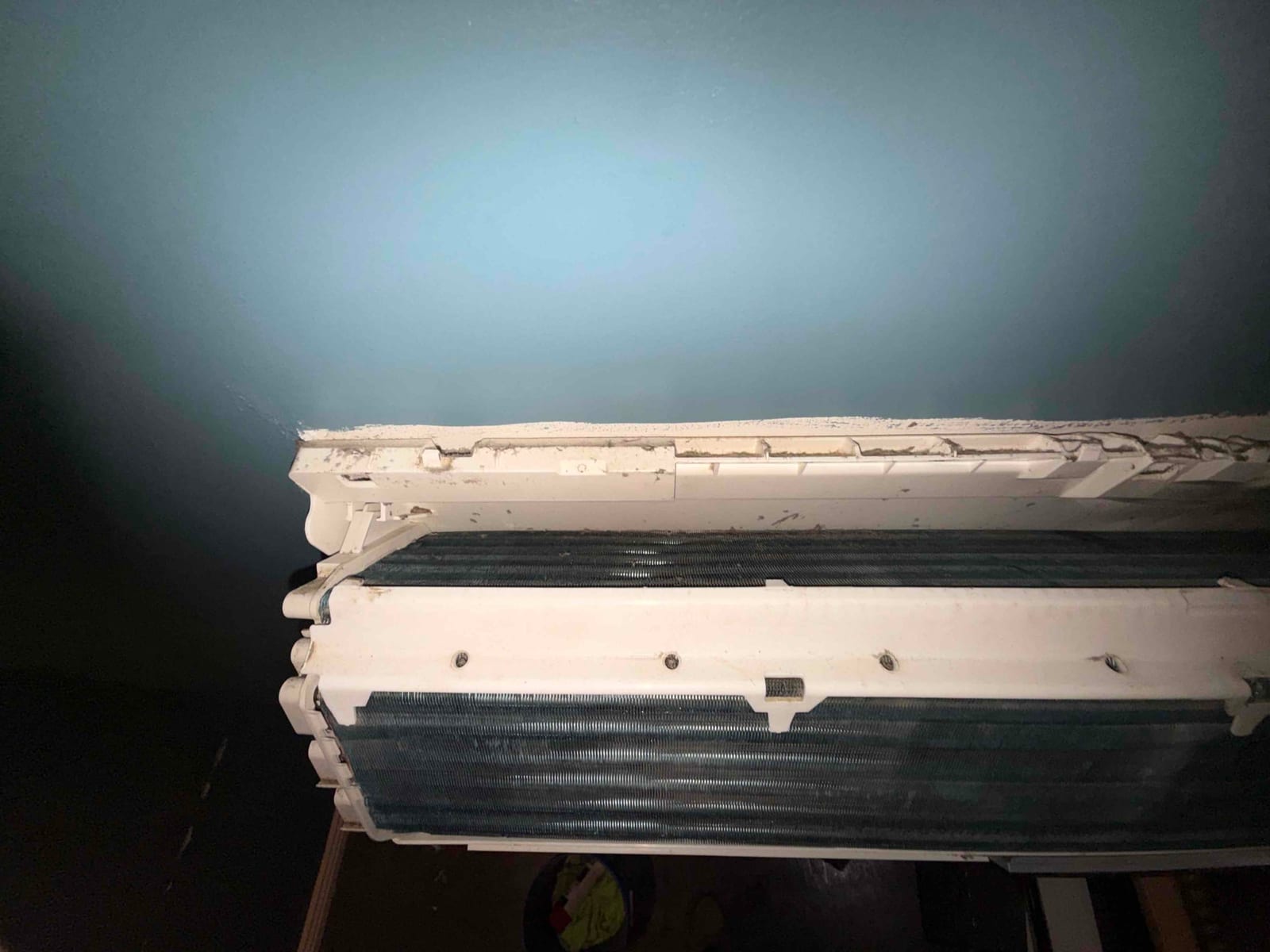 Mini-split indoor evaporator coil with cover removed, showing finned coil surface and surrounding plastic housing during cleaning.