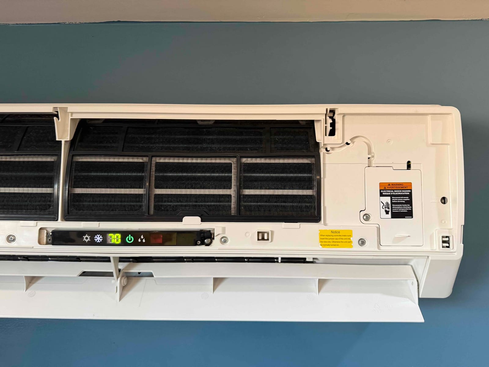 Mini-split indoor unit with front cover open, showing removable air filters and control panel illuminated during coil cleaning.