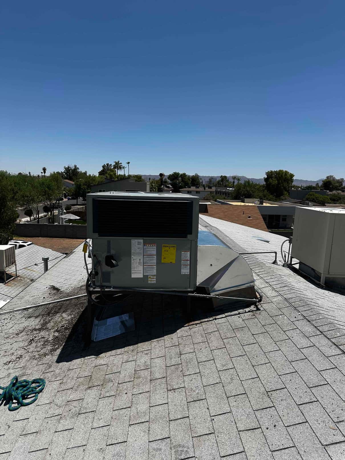 New rooftop package HVAC unit set on curb adapter with connected duct transition and electrical whip visible on the shingle roof.