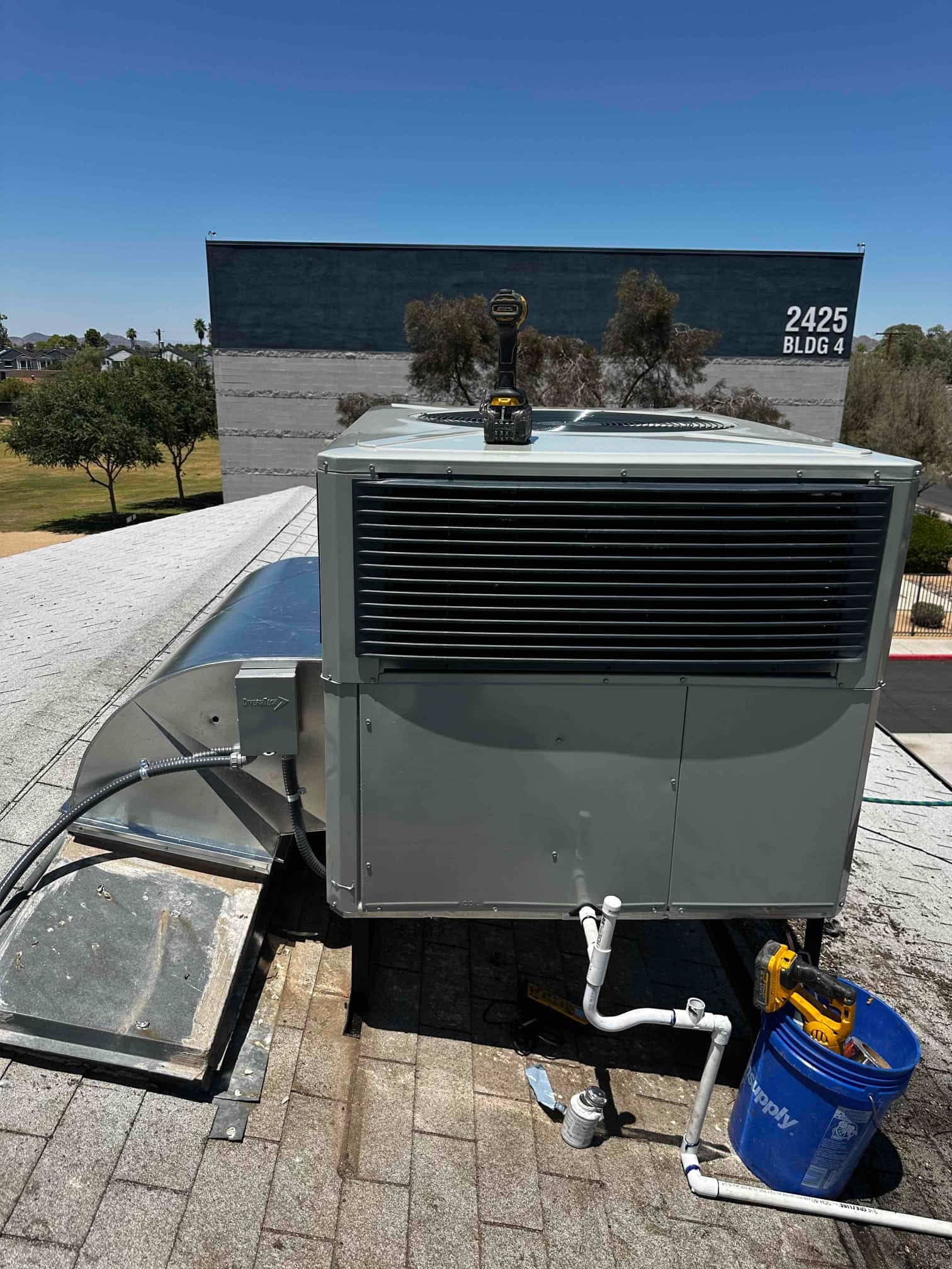 New rooftop package HVAC unit set on curb with connected duct transition, electrical whip, and condensate drain piping.