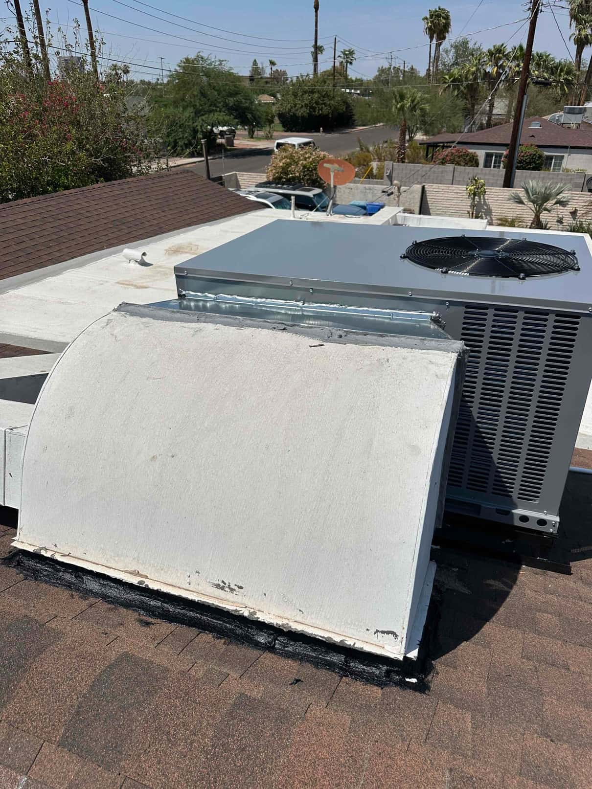 New rooftop package unit set on curb with sealed duct transition and roof penetration, viewed from the shingle roof.