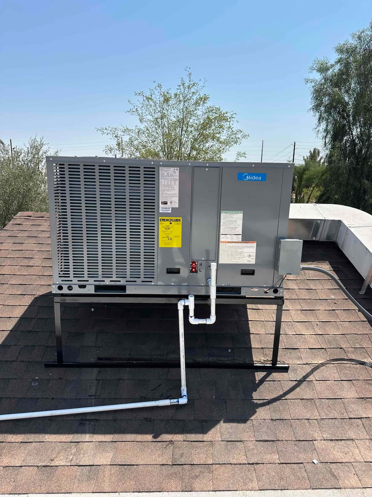 New rooftop package unit set on a stand with connected condensate drain piping and electrical disconnect mounted beside the cabinet.