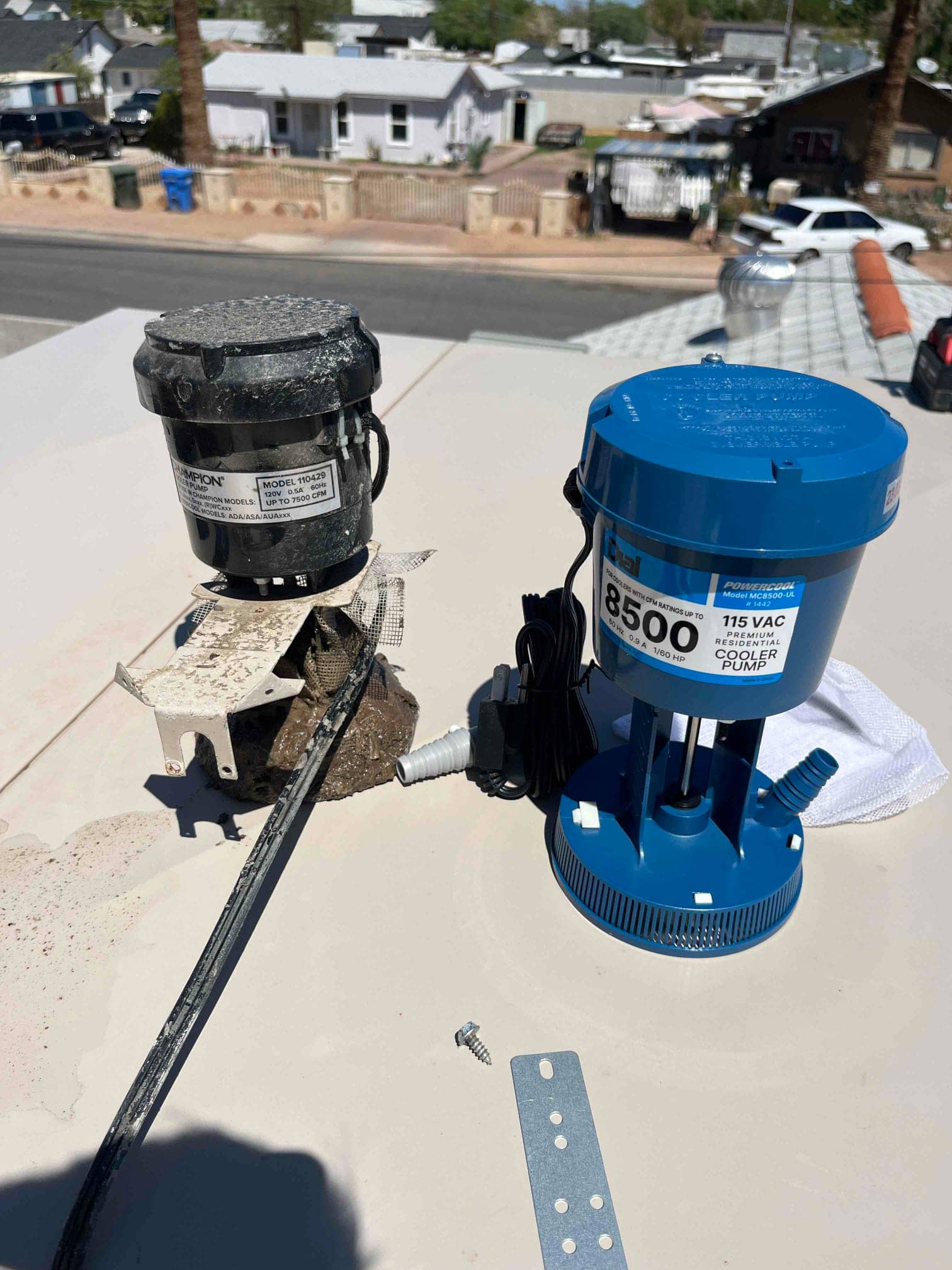 Old evaporative cooler stand pipe assembly removed beside new 115 VAC replacement unit on rooftop, with wiring and mounting hardware visible.