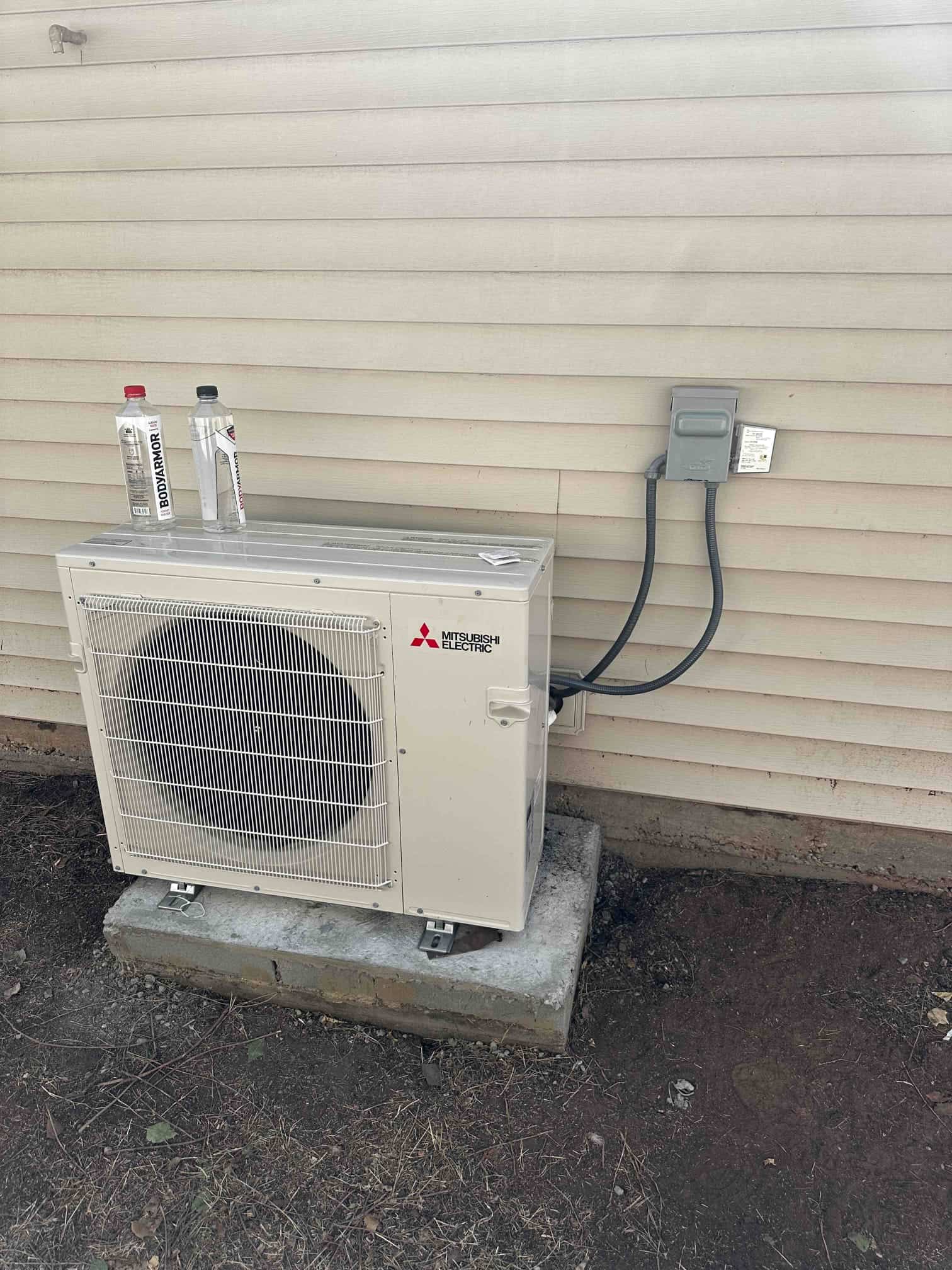 Outdoor mini-split condenser set on a level pad with weatherproof disconnect and sealed line set penetration at the siding.