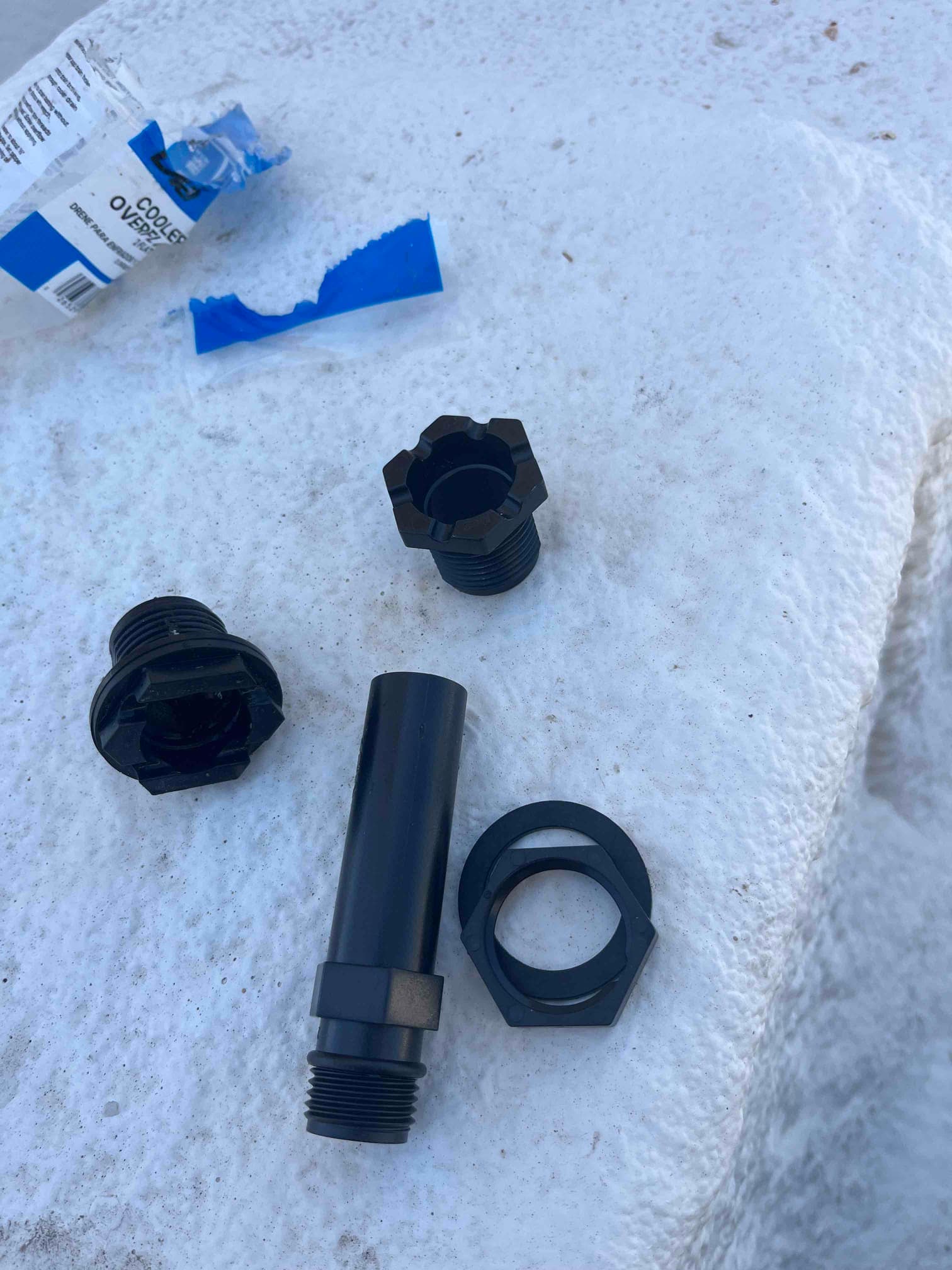 Replacement evaporative cooler standpipe components laid out on the unit surface, including threaded pipe, nuts, and caps.