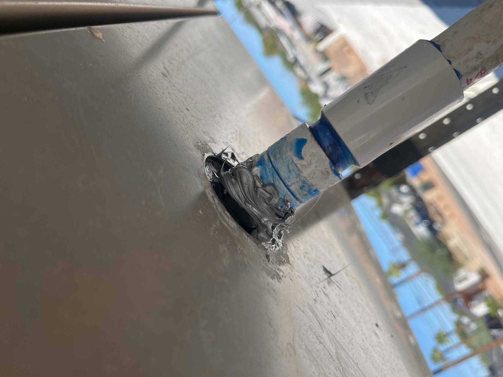 Stand pipe penetration through metal panel sealed with fresh gray sealant around the base of the pipe.