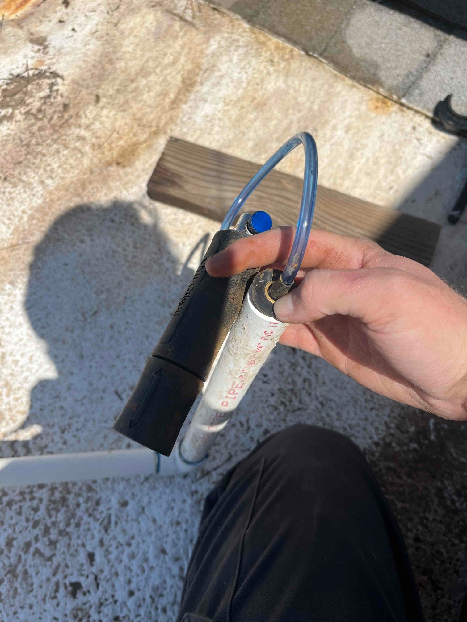 Technician hand holds an evaporative cooler stand pipe assembly with attached tubing on a rooftop during replacement.