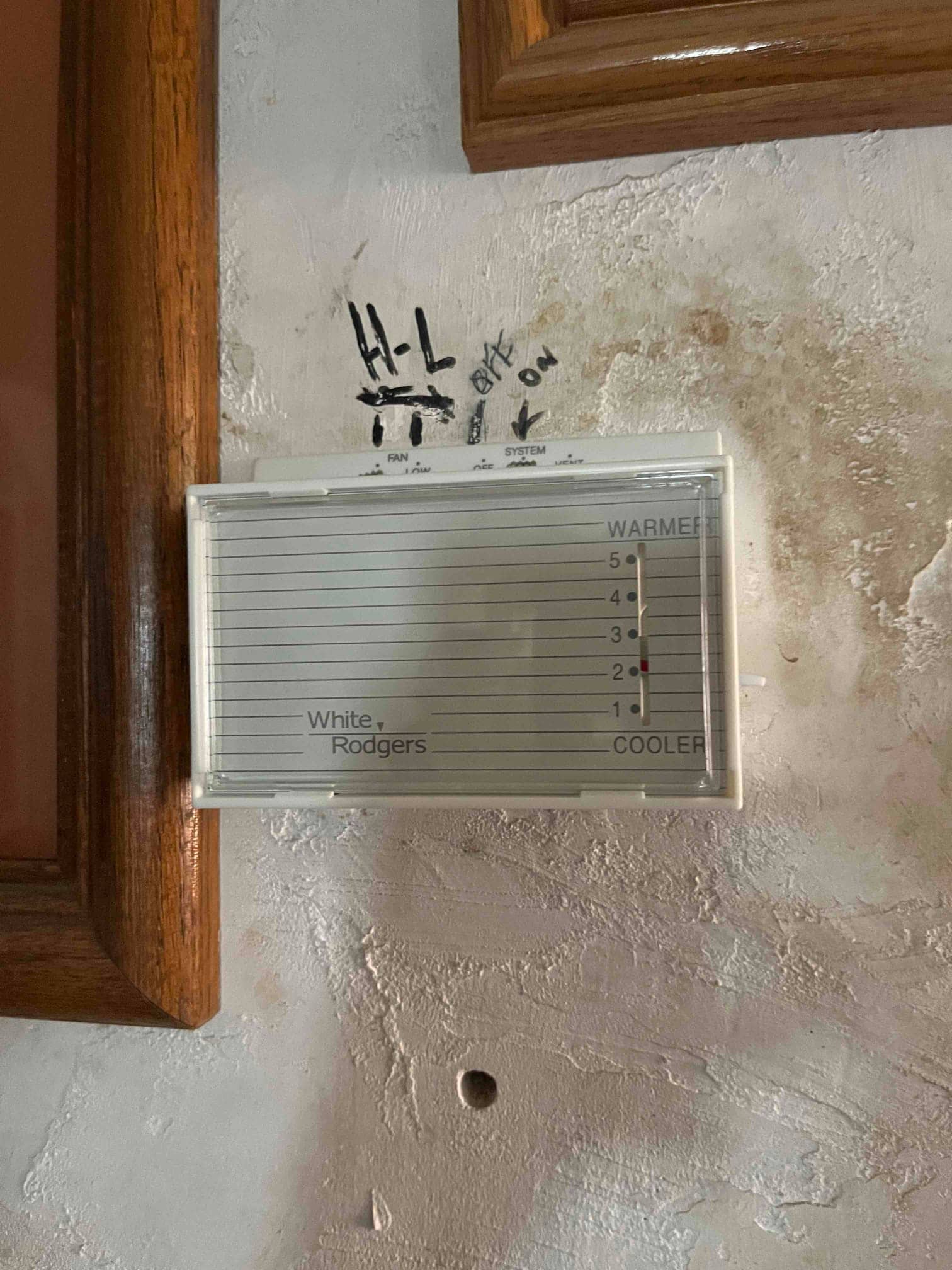 Wall-mounted cooler thermostat with temperature slider and handwritten notes above the control, adjacent to wooden trim.