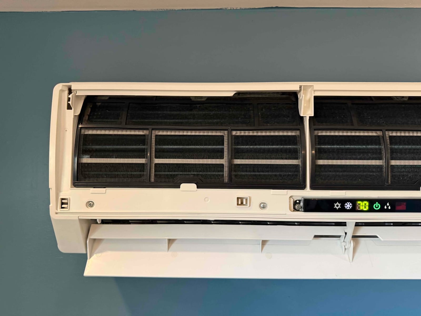 Wall-mounted mini-split air handler with front cover open, exposing evaporator coil and filters during cleaning service.