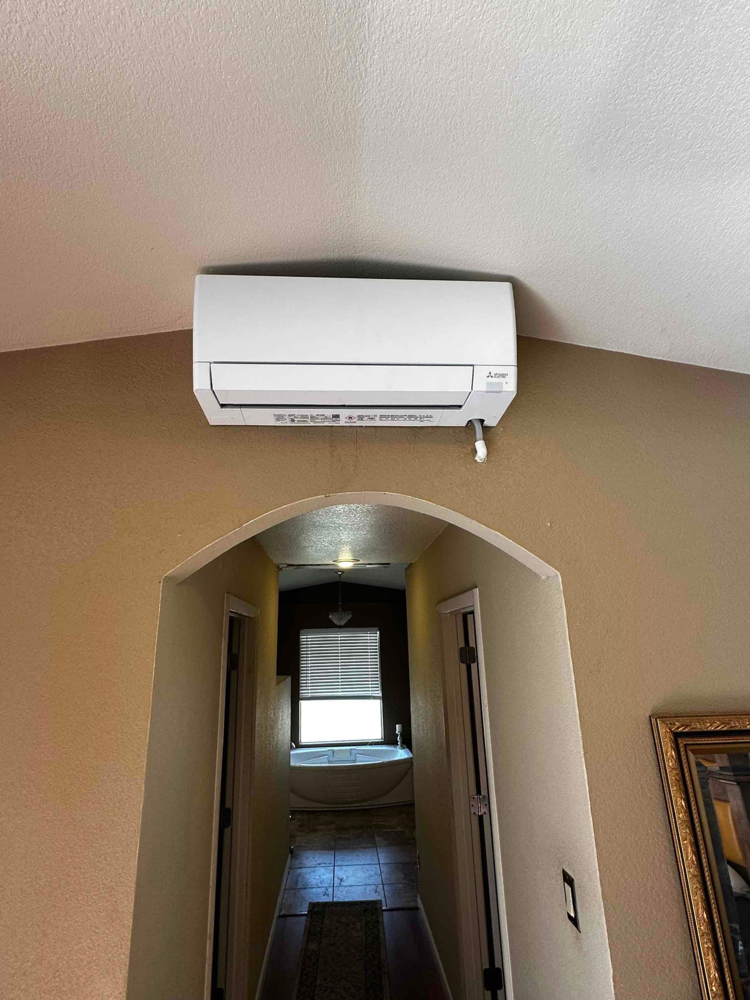 Wall-mounted mini-split indoor unit installed above a hallway arch, with condensate drain outlet visible on the right side.