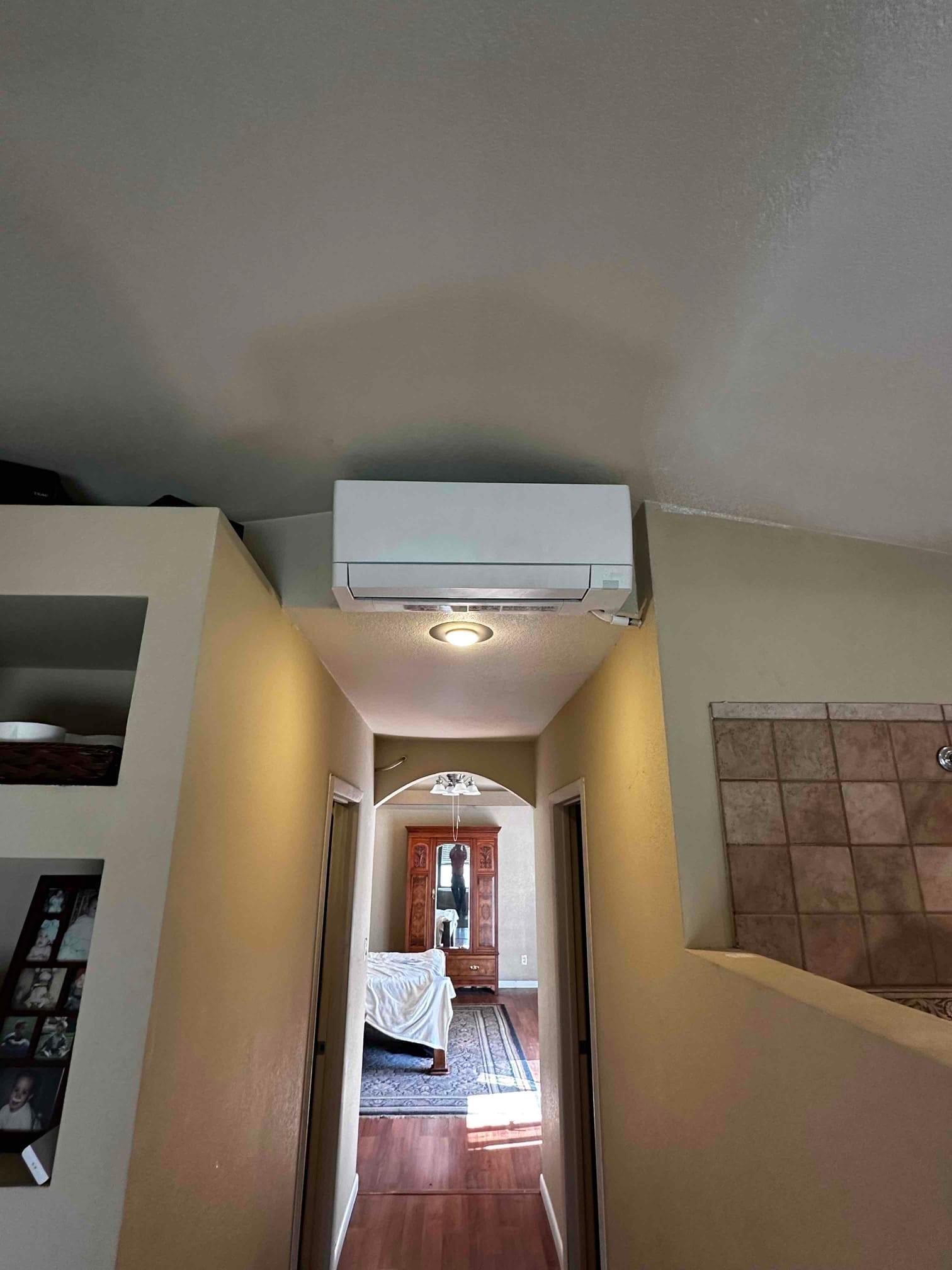 Wall-mounted mini-split indoor unit installed above a hallway ceiling light, showing finished placement and clear airflow path toward the bedroom.