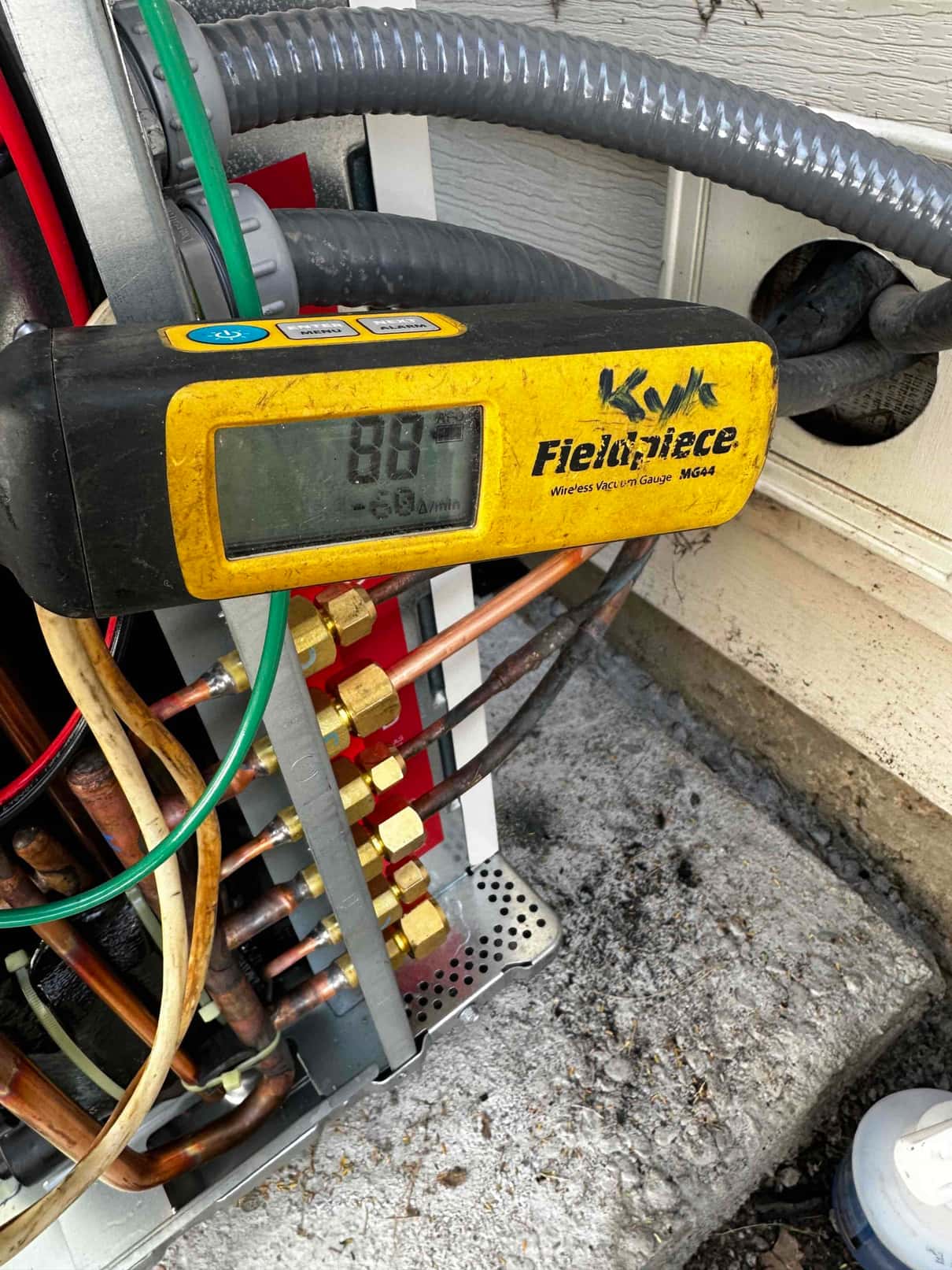Wireless vacuum gauge connected at the outdoor unit shows a deep vacuum below 1000 microns during system evacuation.