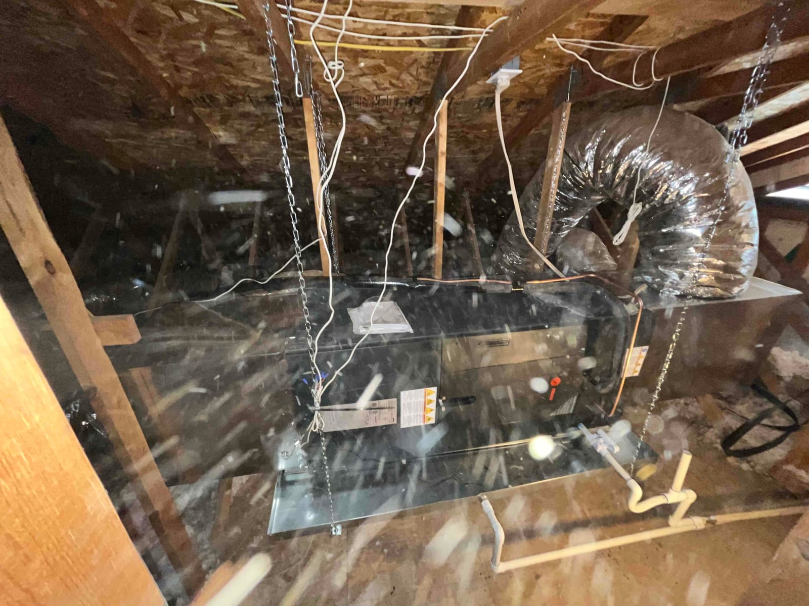 Air handler suspended in attic with flex duct connections, drain piping, and hanging chains visible after installation.