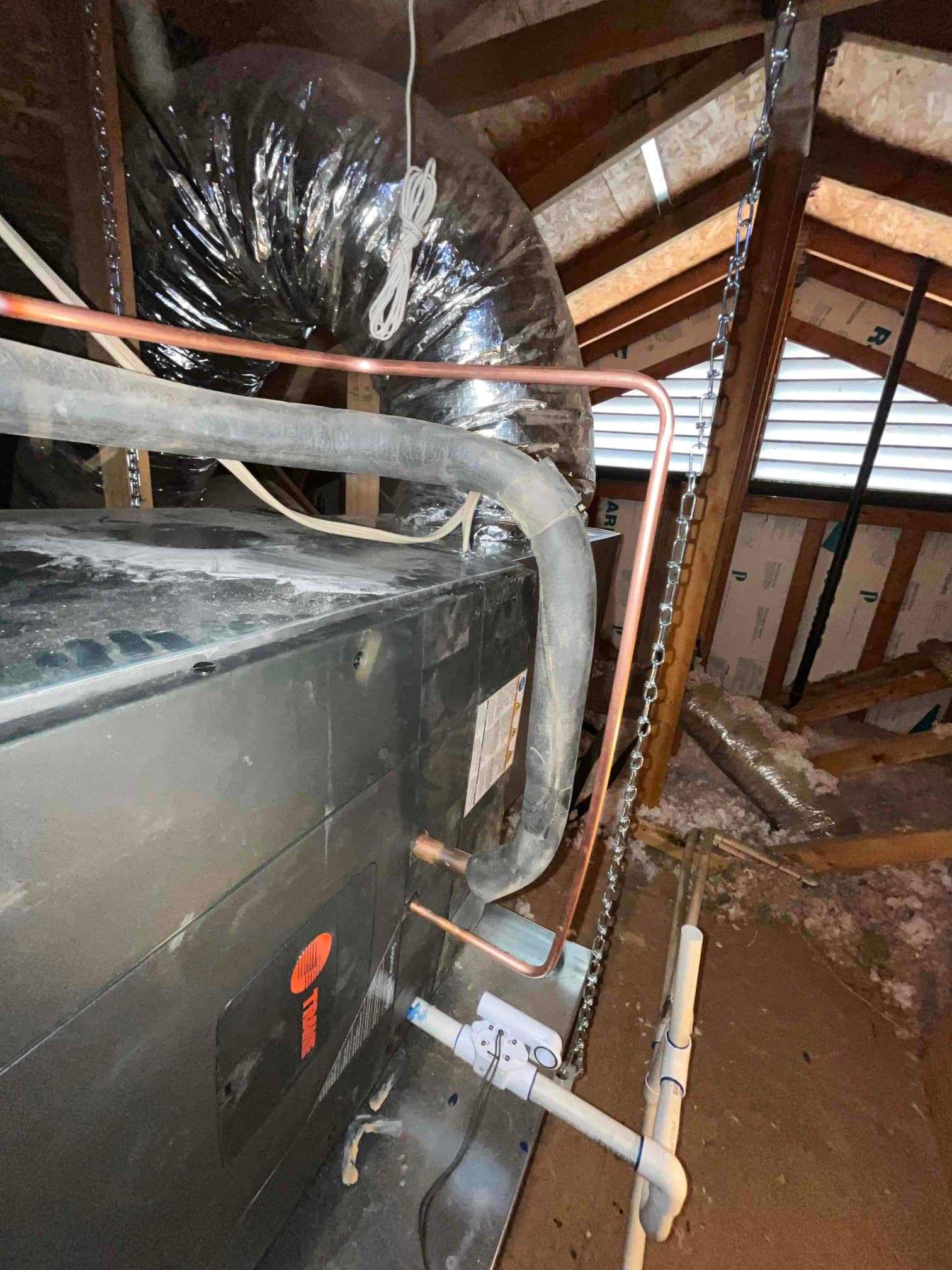Air handler suspended in attic with insulated duct, copper refrigerant lines, and newly plumbed condensate drain with cleanout.