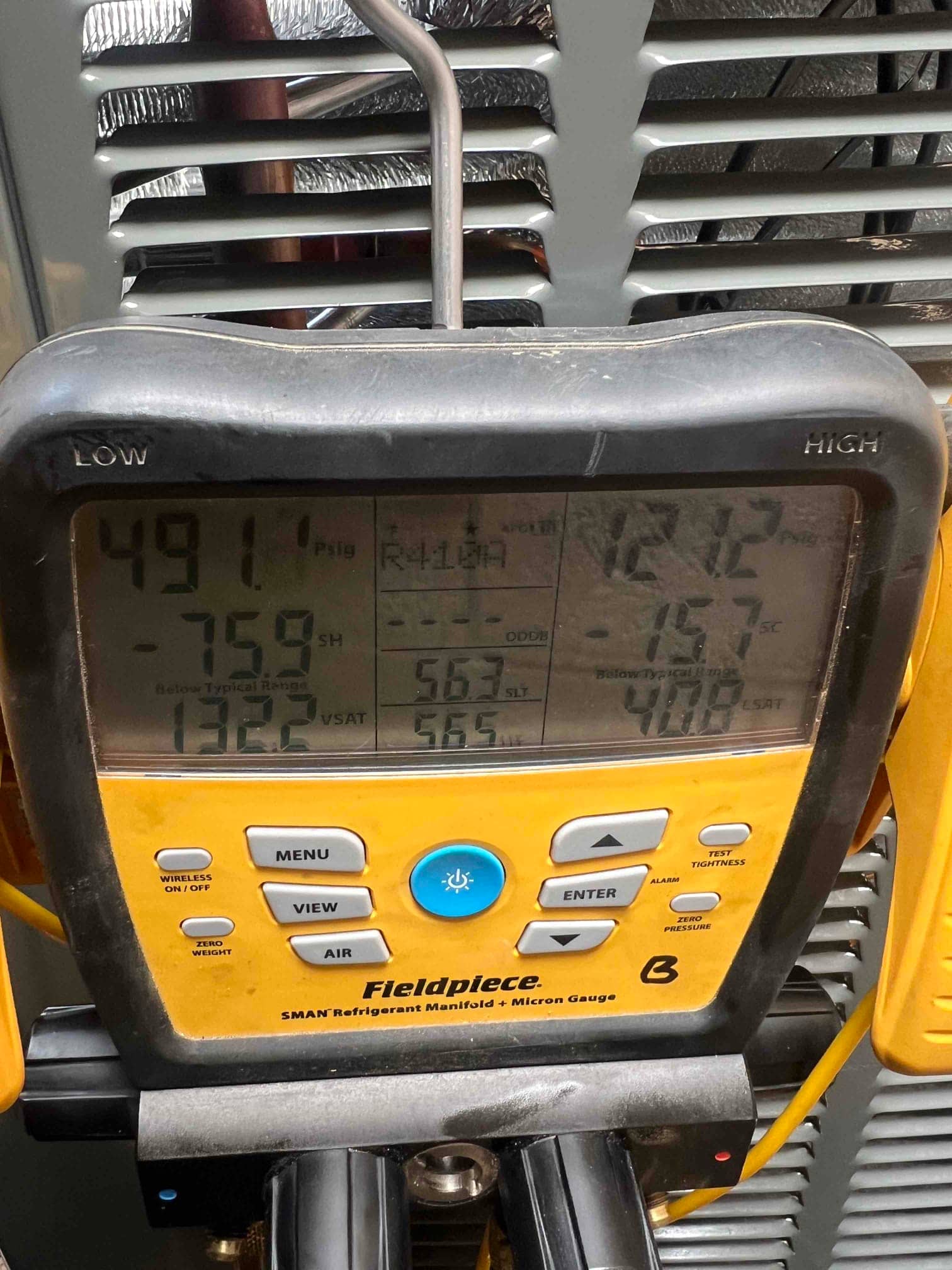 Digital manifold connected at the condenser shows operating refrigerant pressures and temperatures during system commissioning.