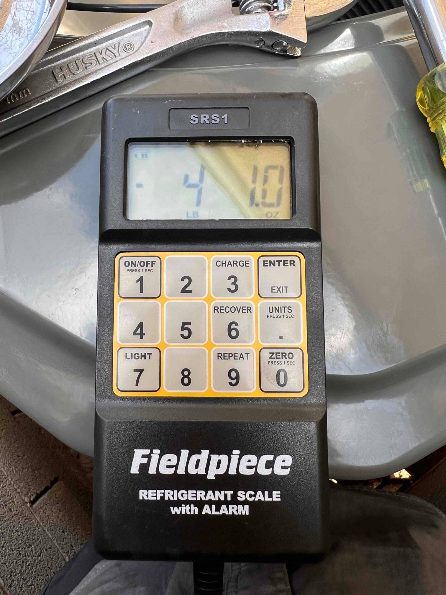 Digital refrigerant scale on the job site displaying 4 pounds 1 ounce during charging operations.