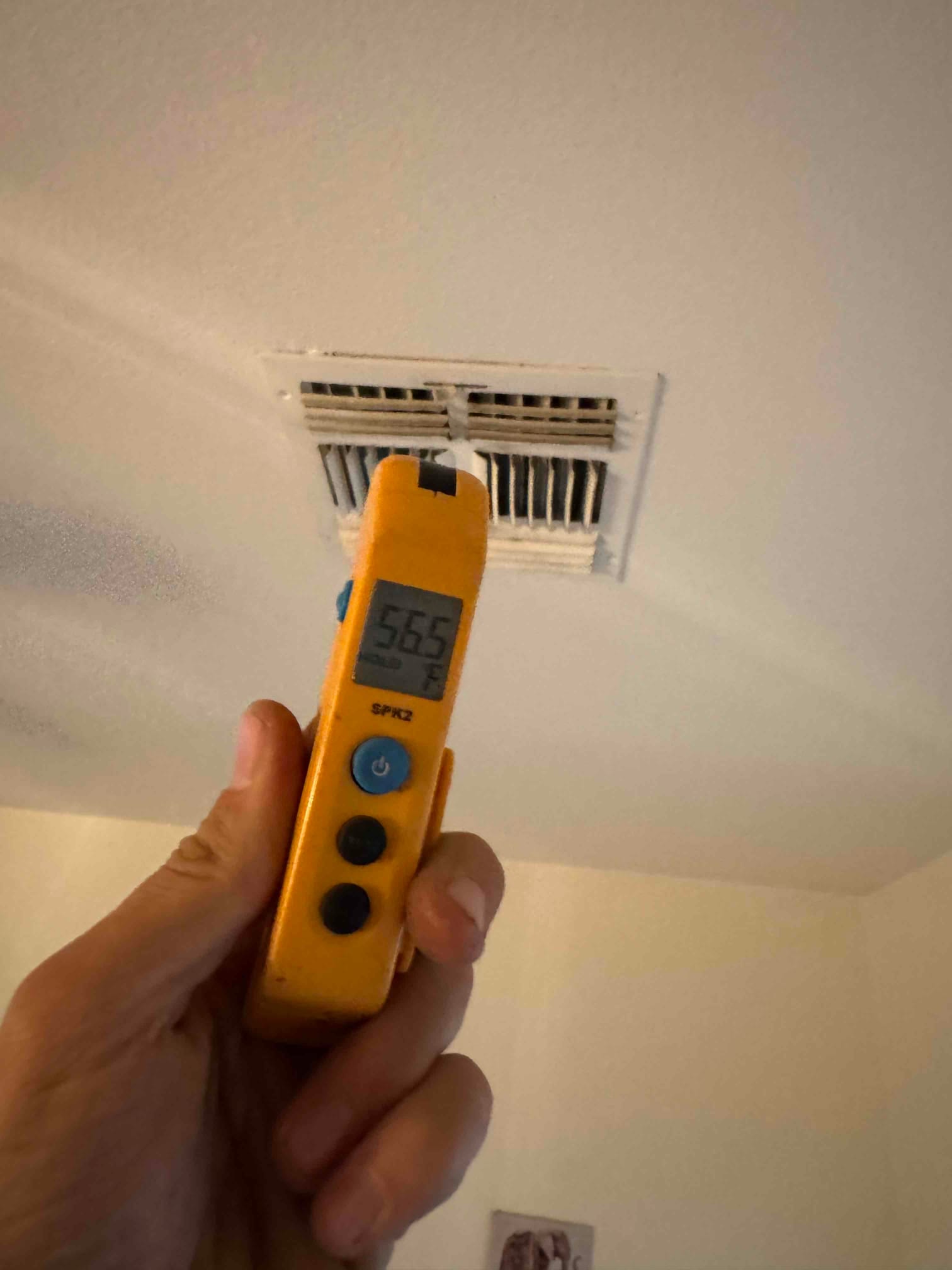 Digital thermometer shows 56.5 °F supply air temperature at the ceiling vent during air conditioner operation.
