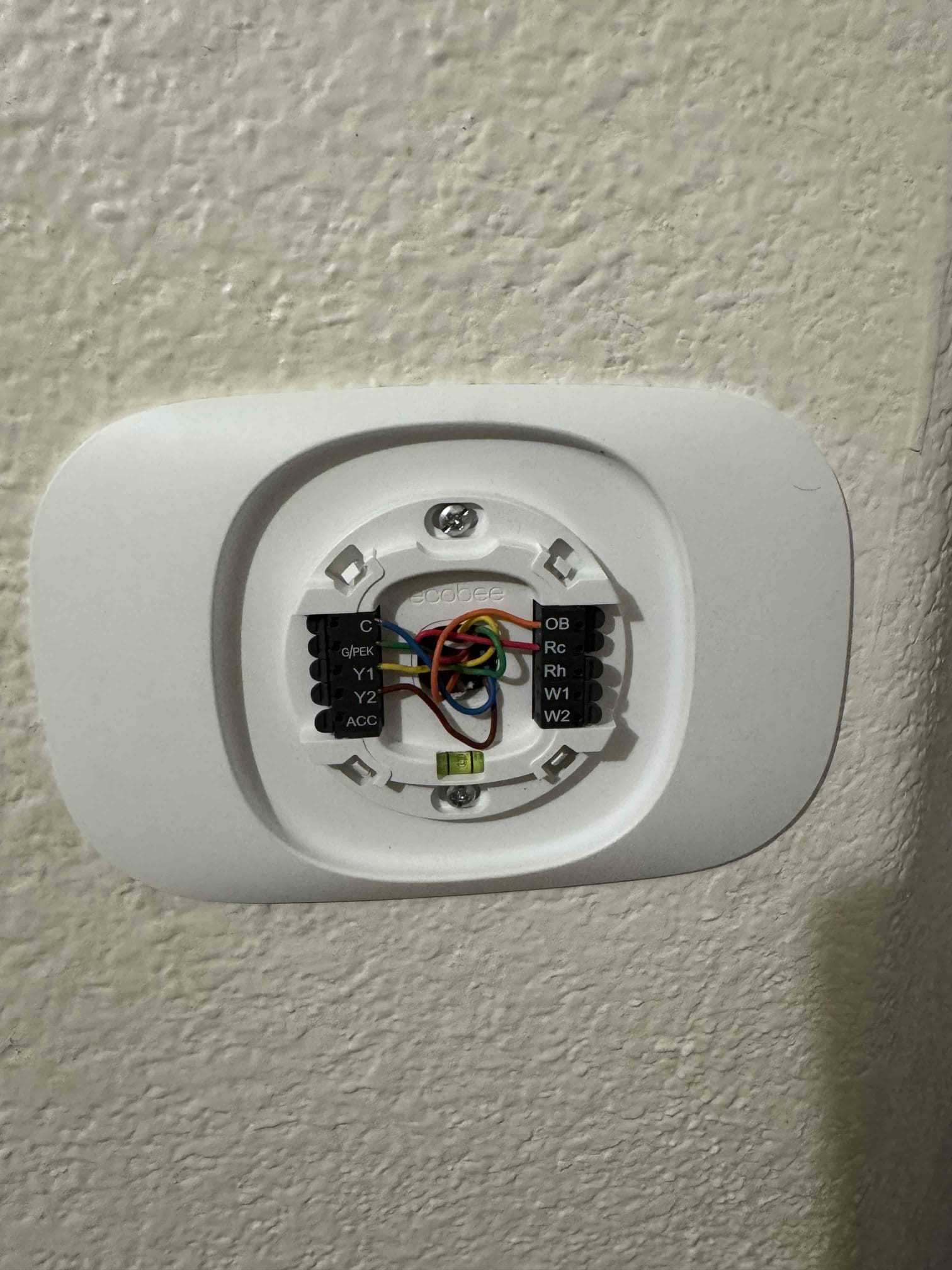 Ecobee thermostat base mounted on interior wall, showing connected control wires labeled C, Rc, Rh, G, Y1, Y2, O/B, W1, and W2.