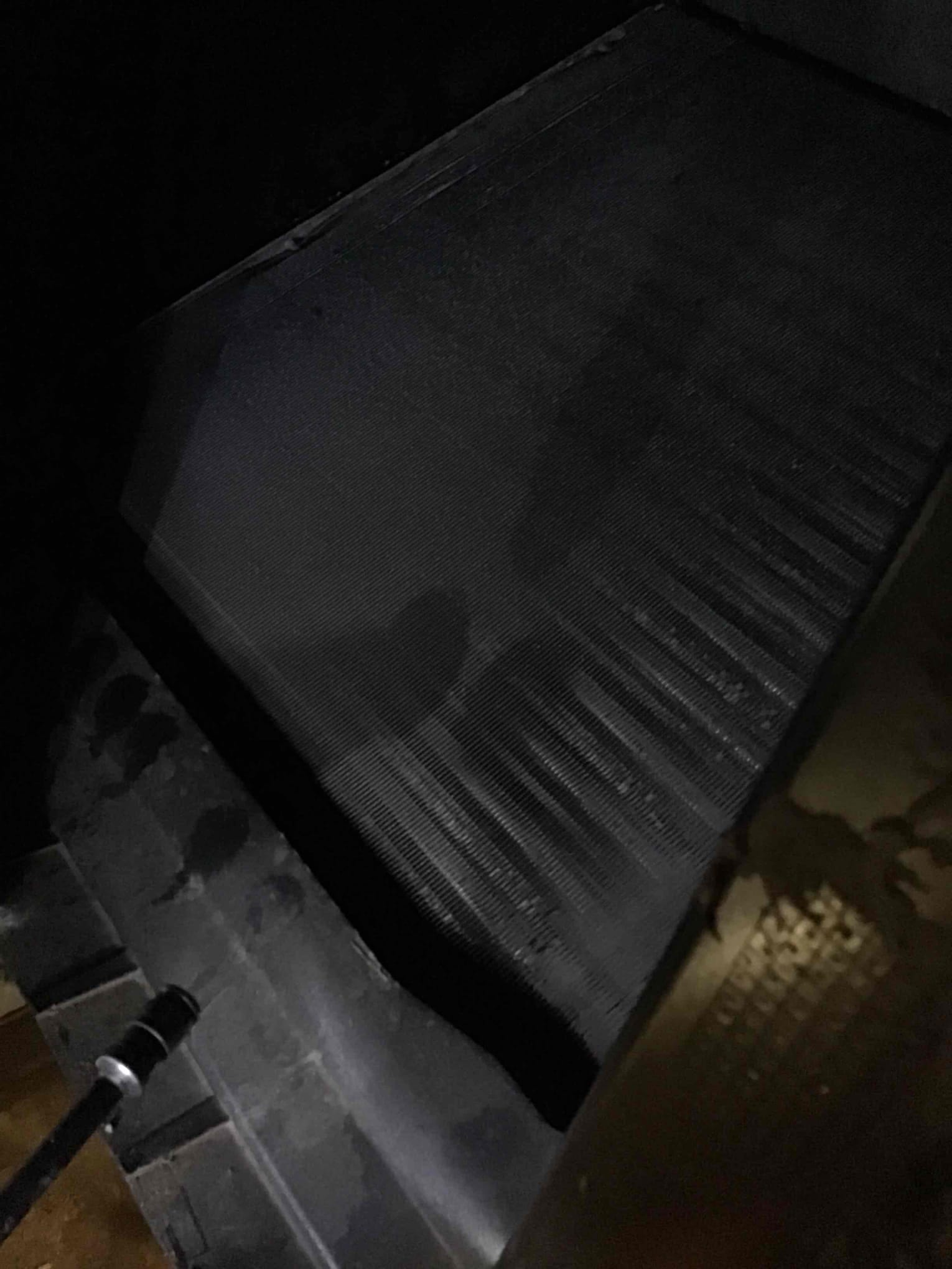 Evaporator coil panel inside the air handler, showing fin surface and surrounding drain pan in low light.