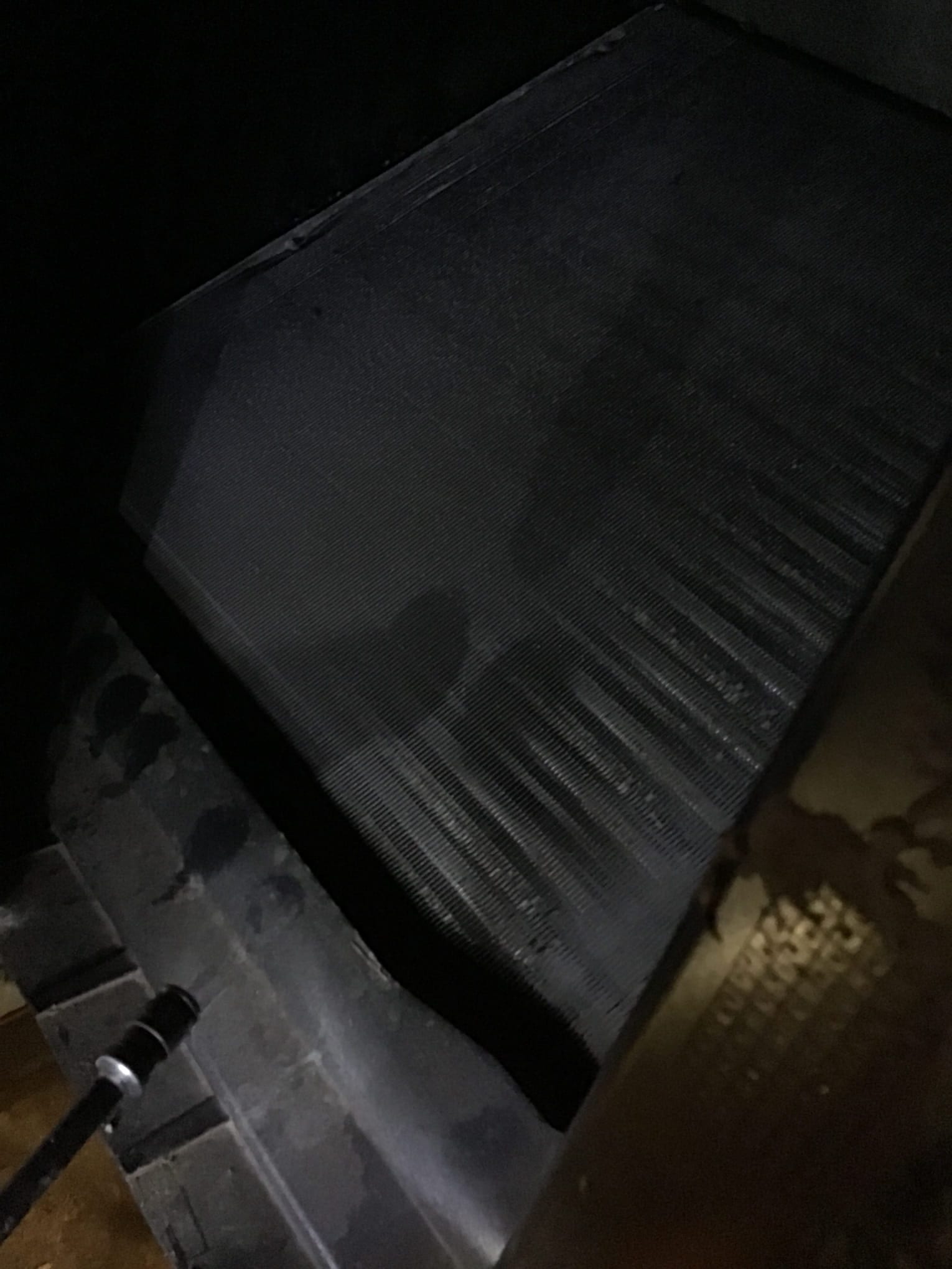 Finned evaporator coil surface inside the air handler, shown close-up with flashlight for visibility.
